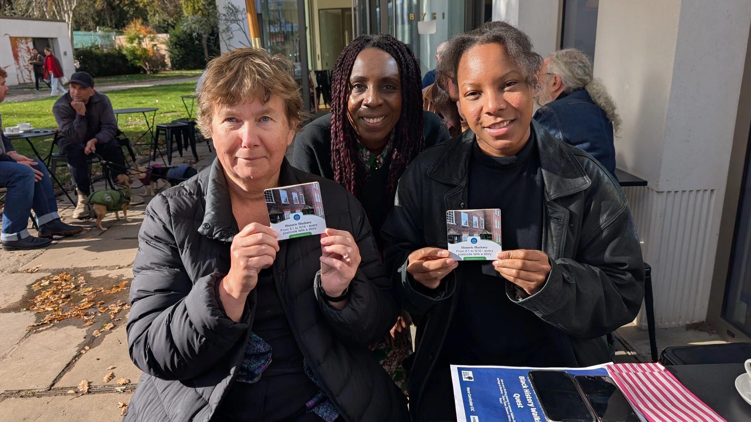 Three women sitting side by side holding up a coaster