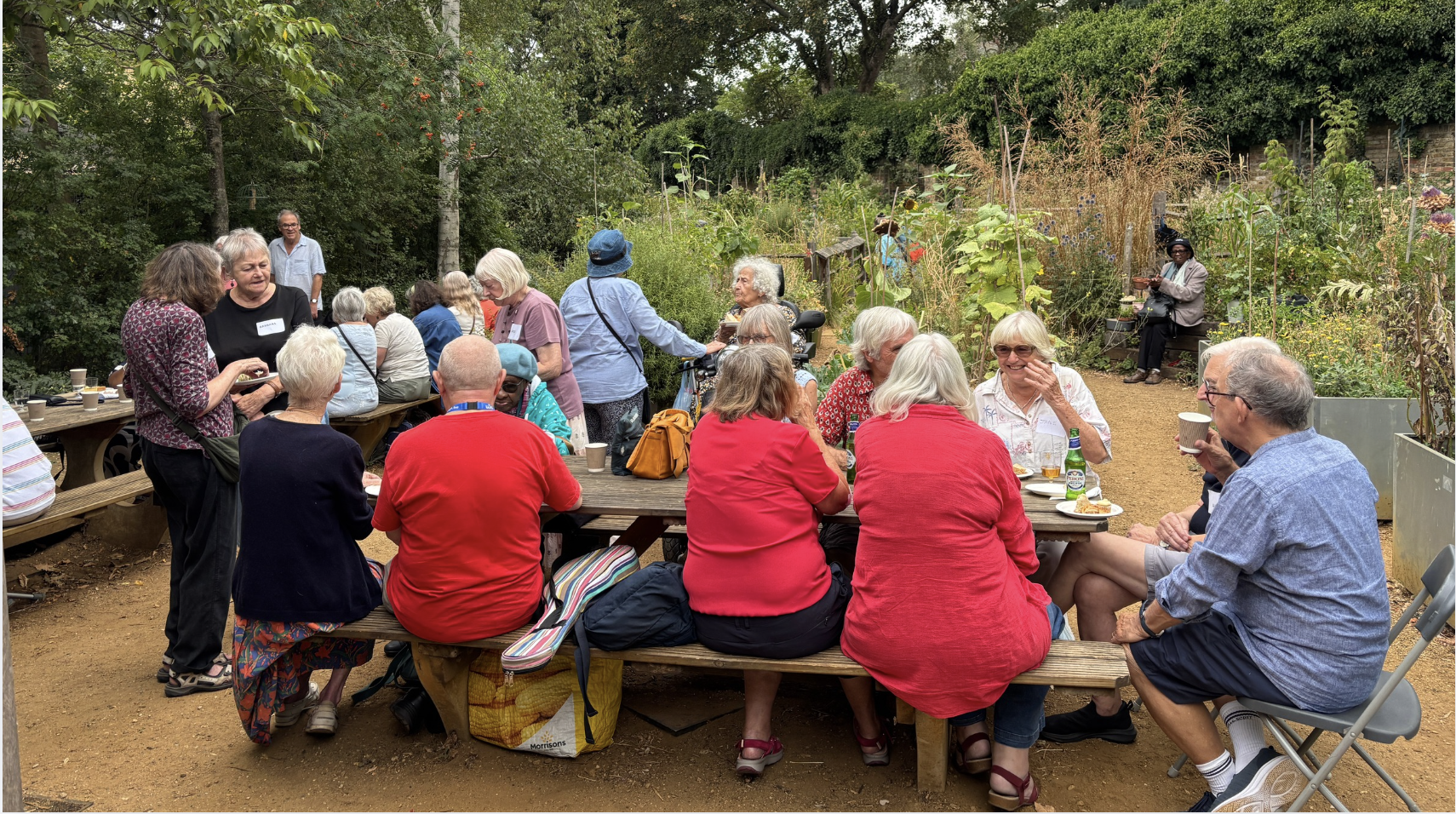 A group of older people sit on some picnic benches