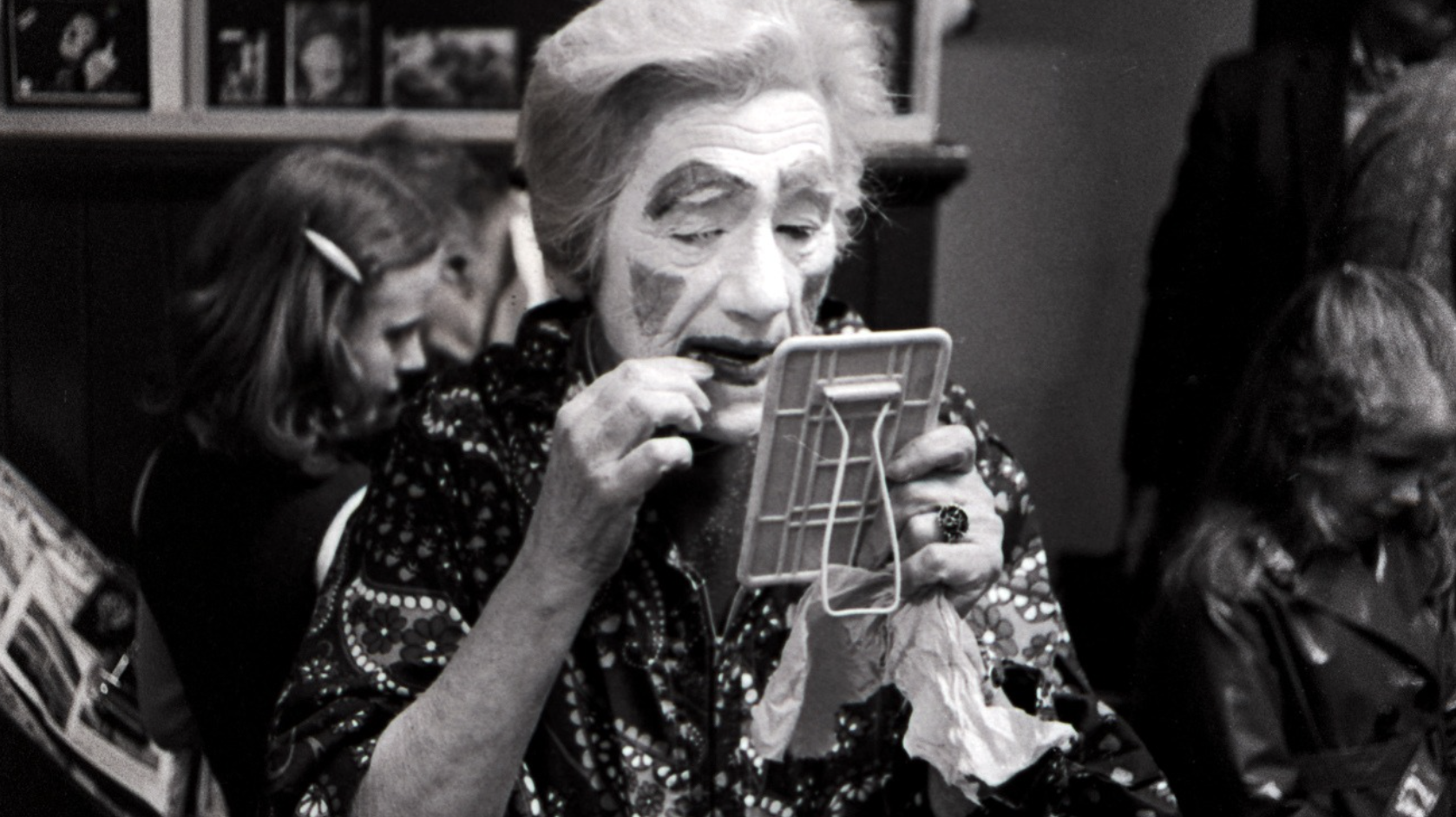a black and white photo of a clown applying make-up