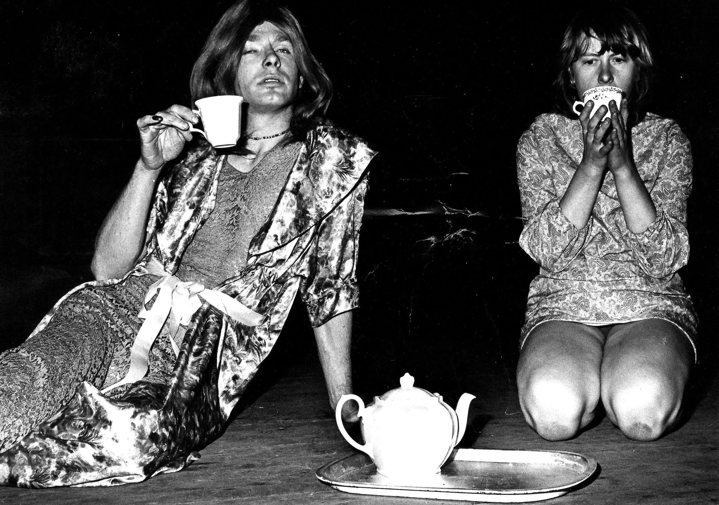 Two people lounge around drinking cups of tea in fancy bed wear