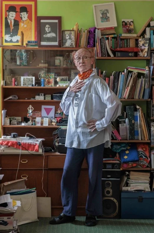 The artist Lavinia Co-op poses for the photo at home, surrounded by books, framed images and multiple items on shelves