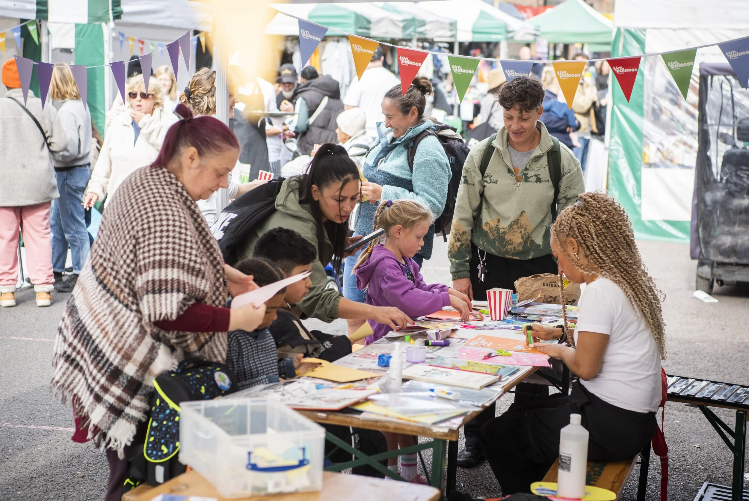 A group of shoppers in Hoxton Street Market take part in some craft activities at a stall.