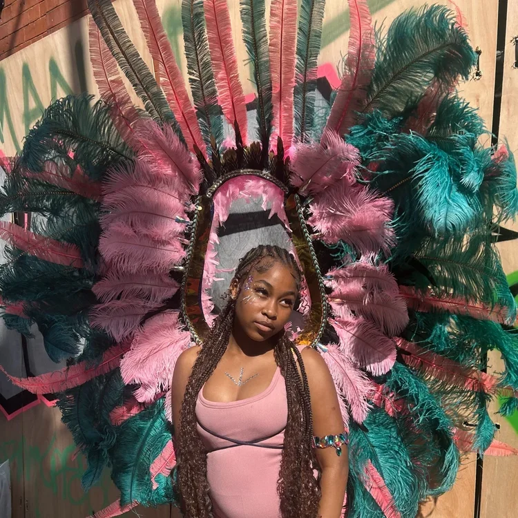 A woman with long braids wears a huge pink and green feather harness