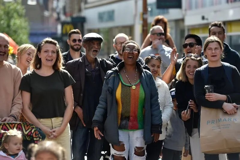A group of people smiling and cheering on a street, as if watching a performance that is out of sight