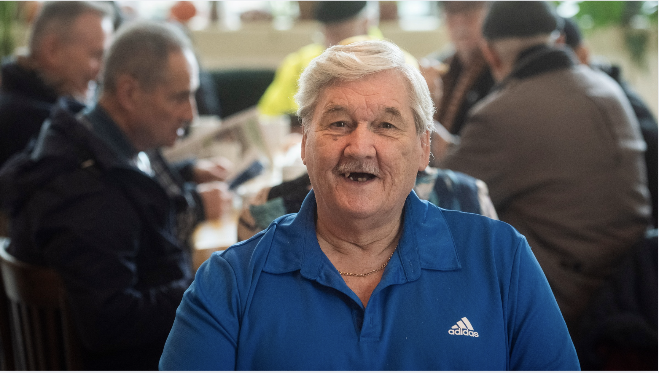 an older man in a blue top with white hair and missing teeth