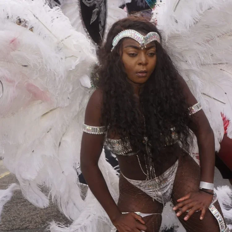 A young woman dancing in a silver bikini and large white feather headdress