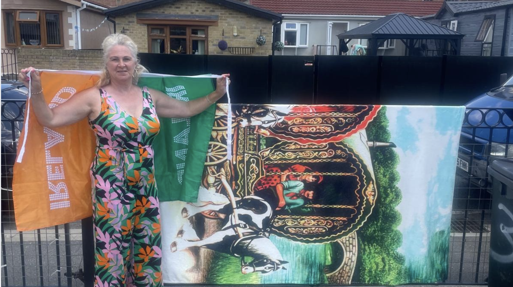 A woman stands in front of a colourful backdrop with a flag draped around her shoulders