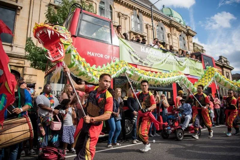 A giant paper dragon being paraded through the streets at the carnival, as if it is flying. A man holds a pole, each holding up a part of the dragon.