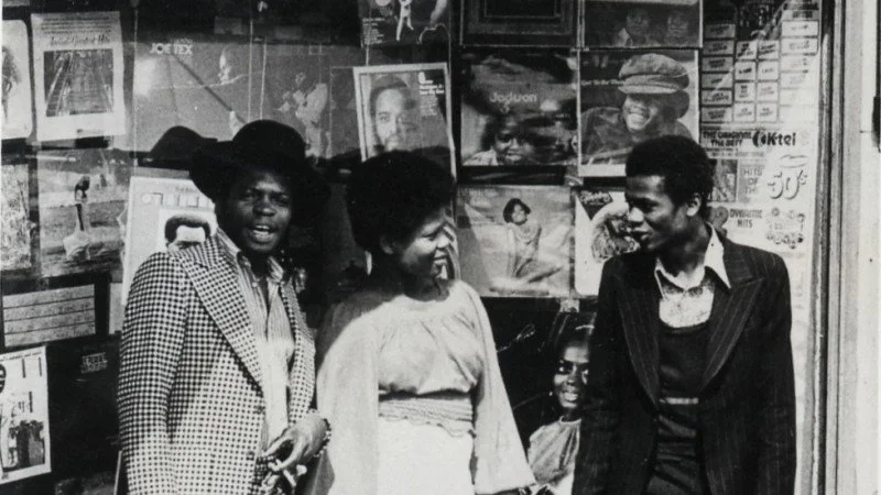 A black and photo of four people - two men, one woman and a child stood in front of a record shop