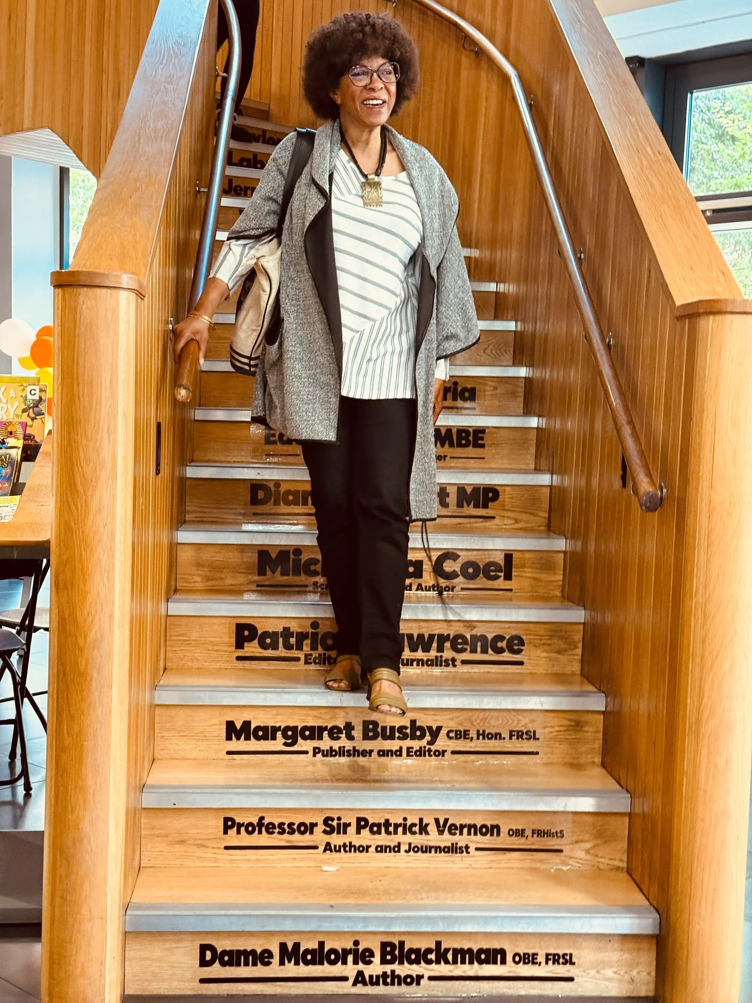 Margaret Busby smiling on the Legacy Steps at Dalston’s CLR James Library, standing above her name.