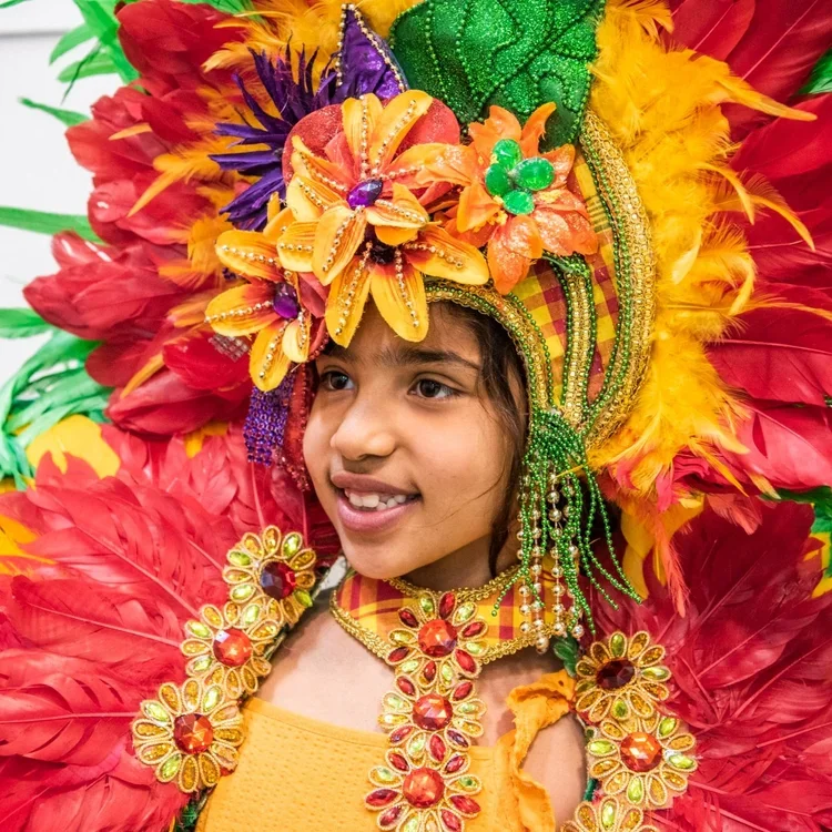 A young girl in an extravagant red and orange headdress with flowers and feathers