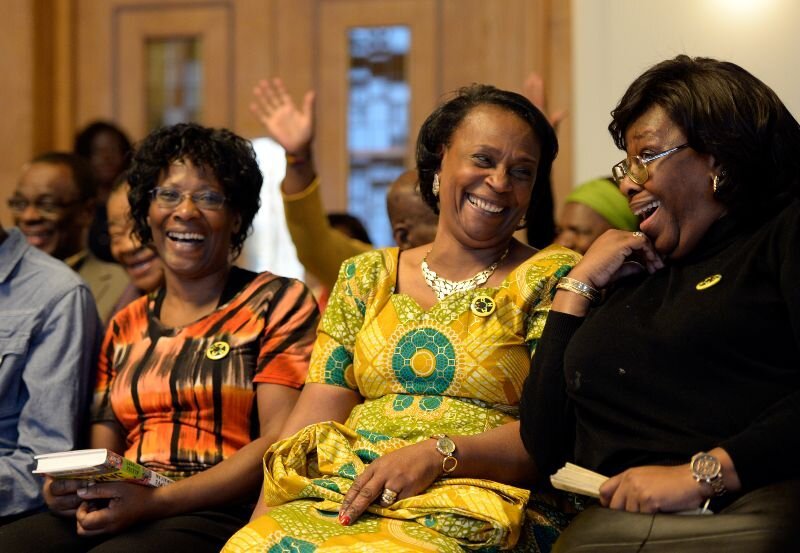 Three women sitting in what appears to be a hall or church down smiling and laughing at each other.