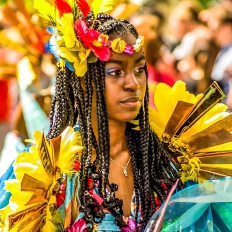 A young woman with dark braids is dresses in a multicoloured floral headress and epaulettes