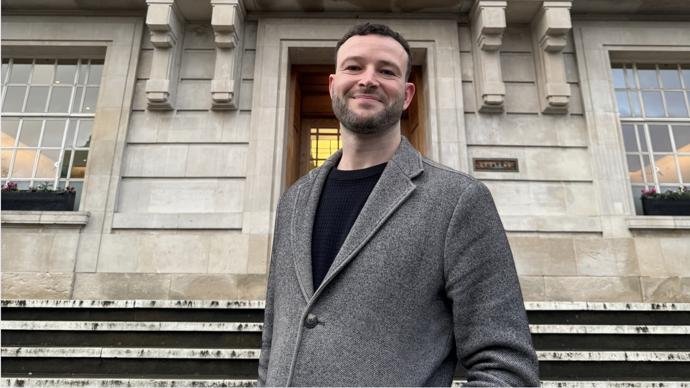 A man in a grey jumper in front of a building
