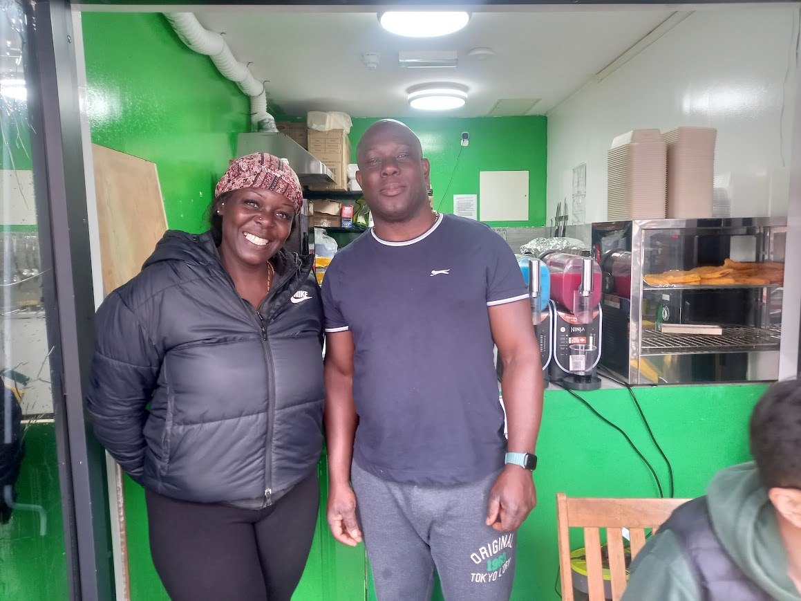 Two people wearing black and standing in front of a green shop