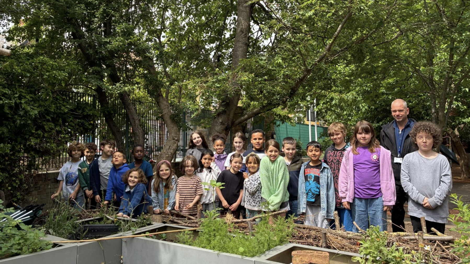 A group of children and adults stand ina shaded garden