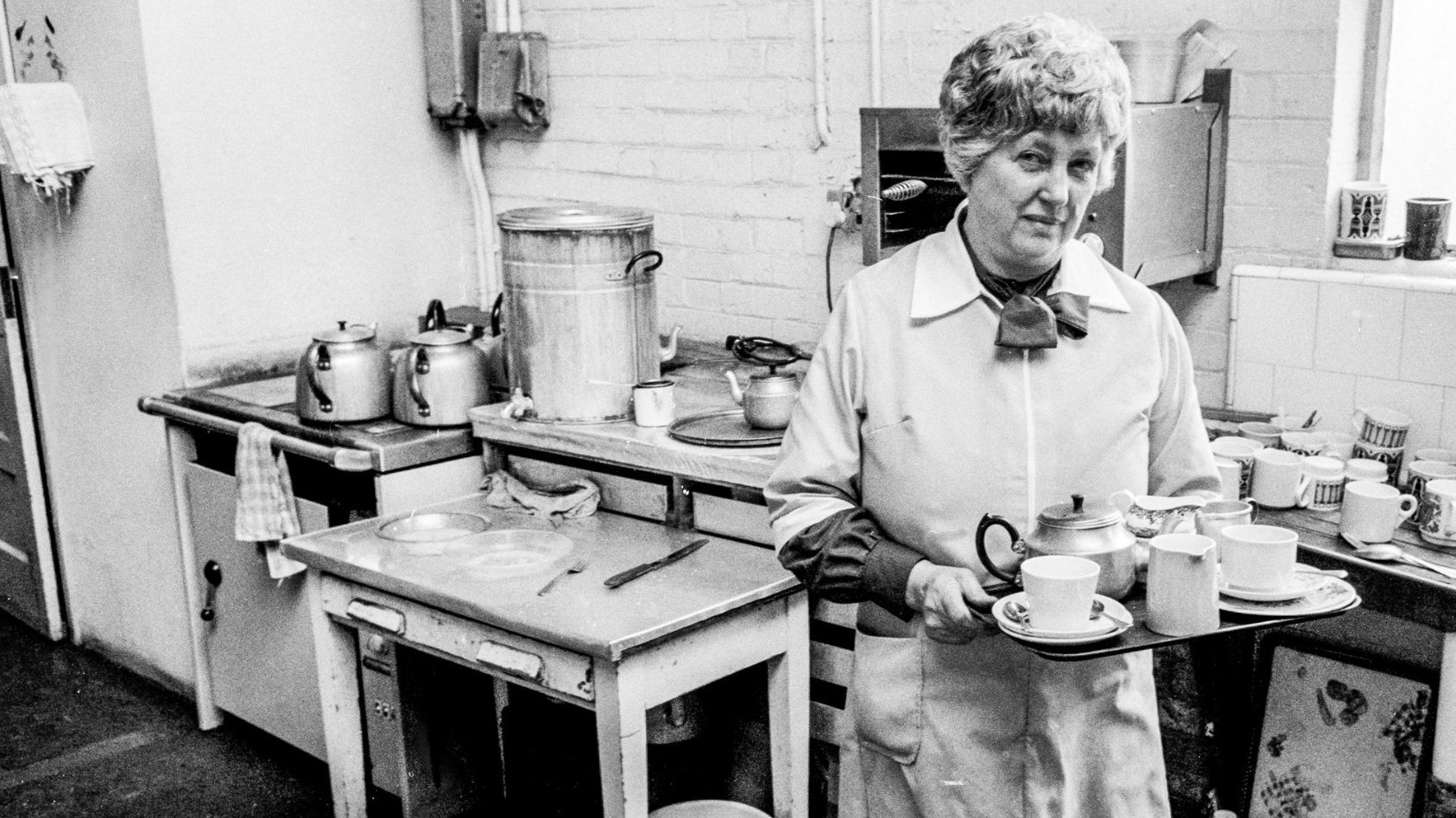 a black and white image of a lady holding a tray of tea