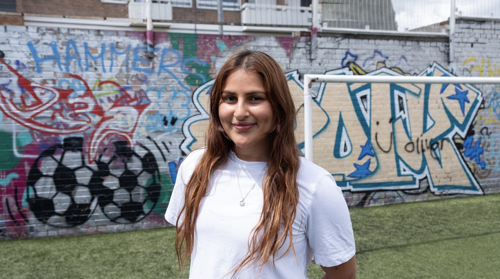 A woman stands in front of a wall of graffiti