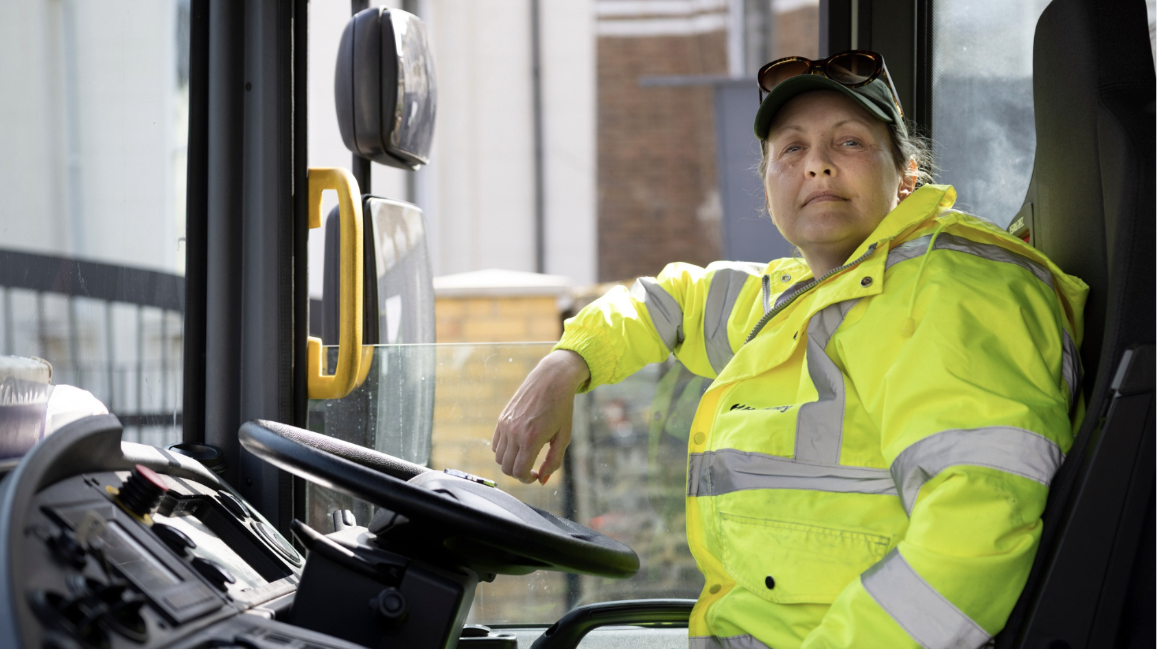 a woman in a high-vis jacket sits behind a steering wheel