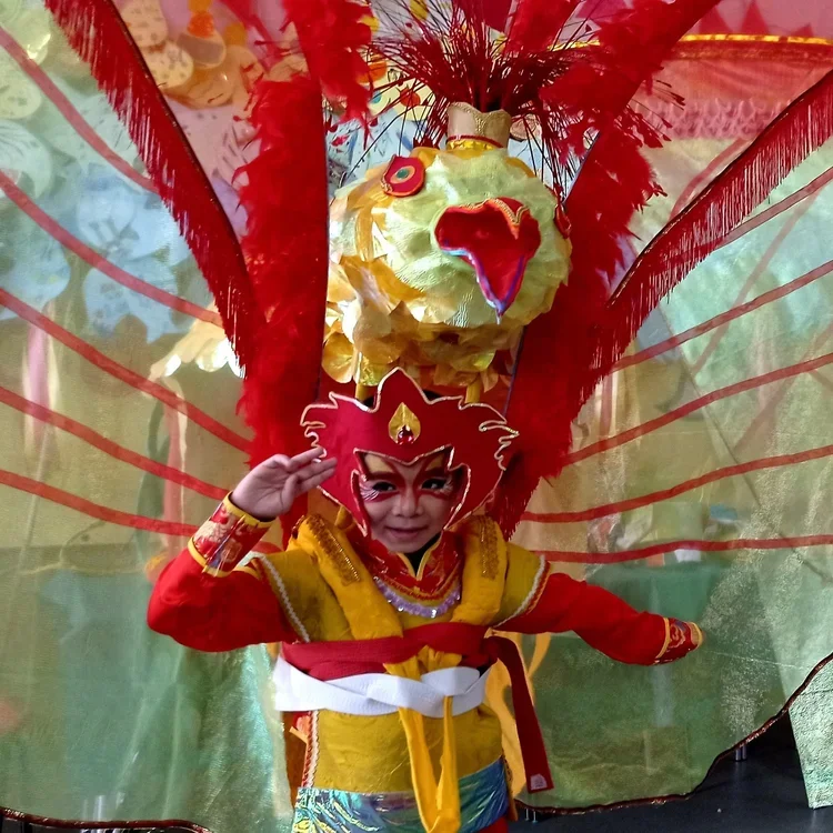 A child salutes dressed in a large red and yellow costume with wings