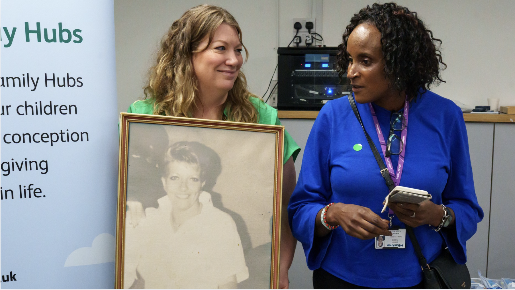 two women talking, while a woman holds up a black and white portrait of a woman