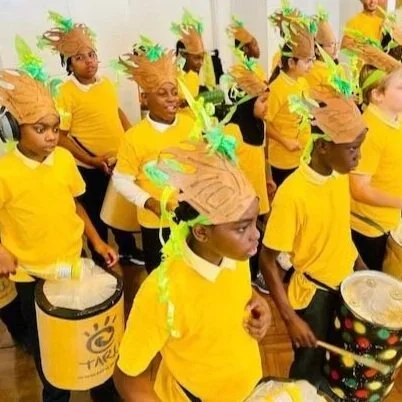 A group of boys dresses in yellow with brown and green headdresses while playing drums
