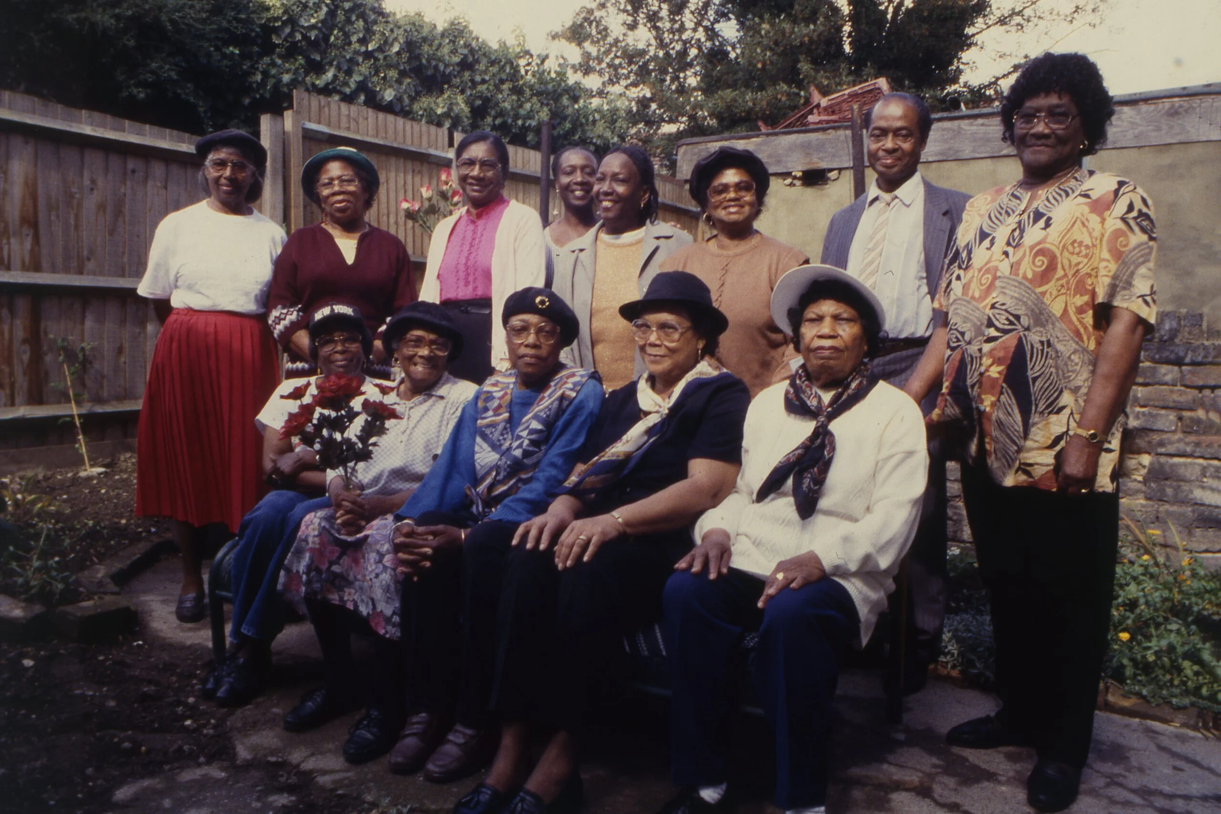 A group photo of older Afro-Caribbean people in a garden. One row of people are seated at the front, others stand behind in a line.