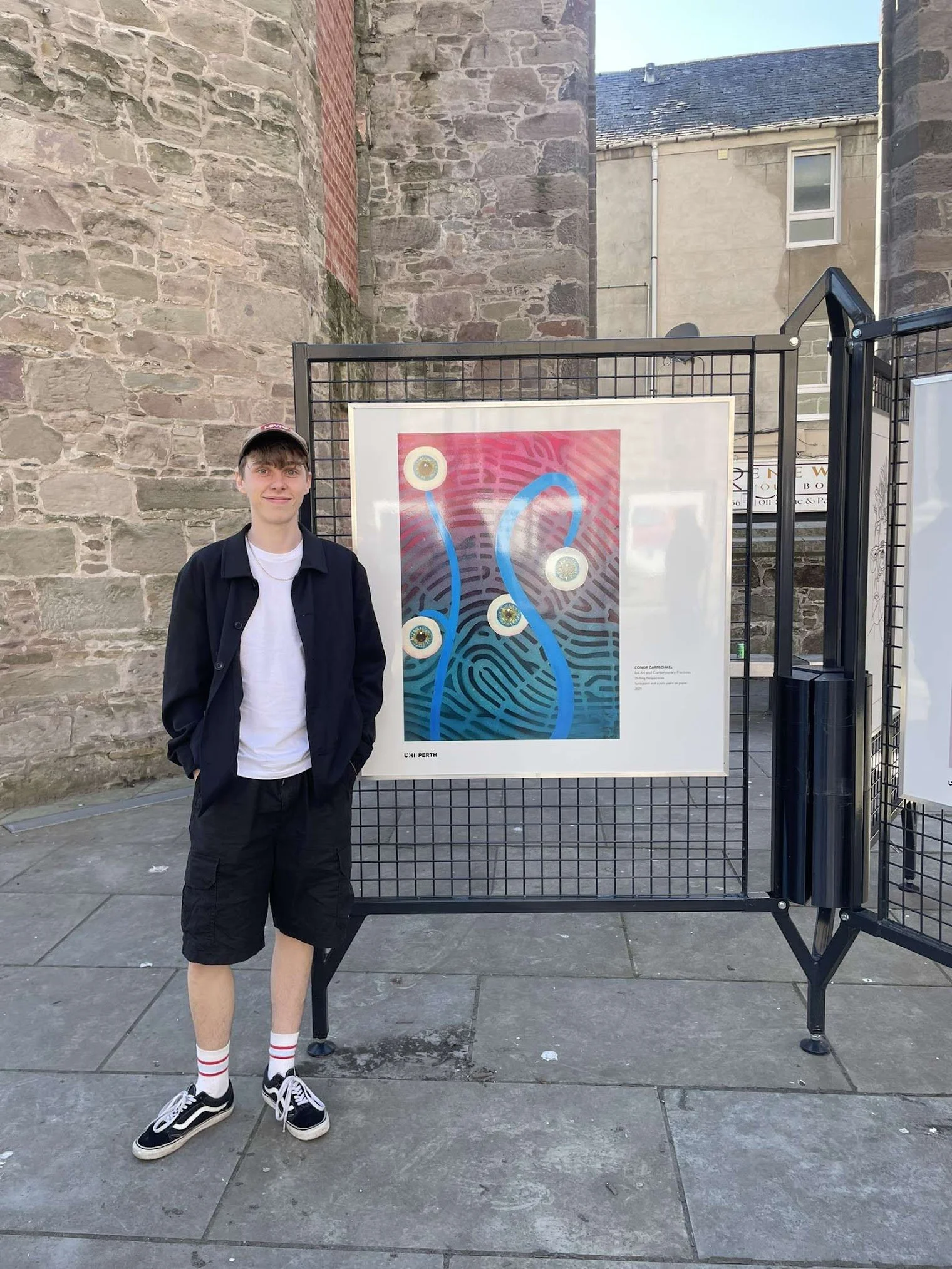 An artist standing next to abstract art on an outdoor display.