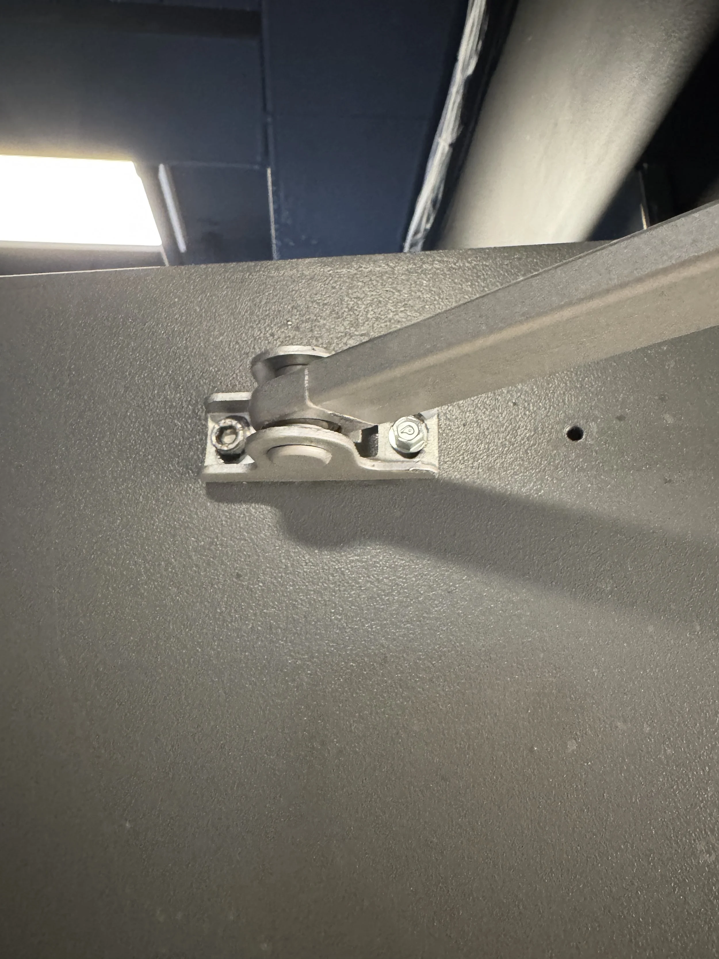 Nærbilde av en hengsling på en metalloverflate, med skruer og en støtteleppe.