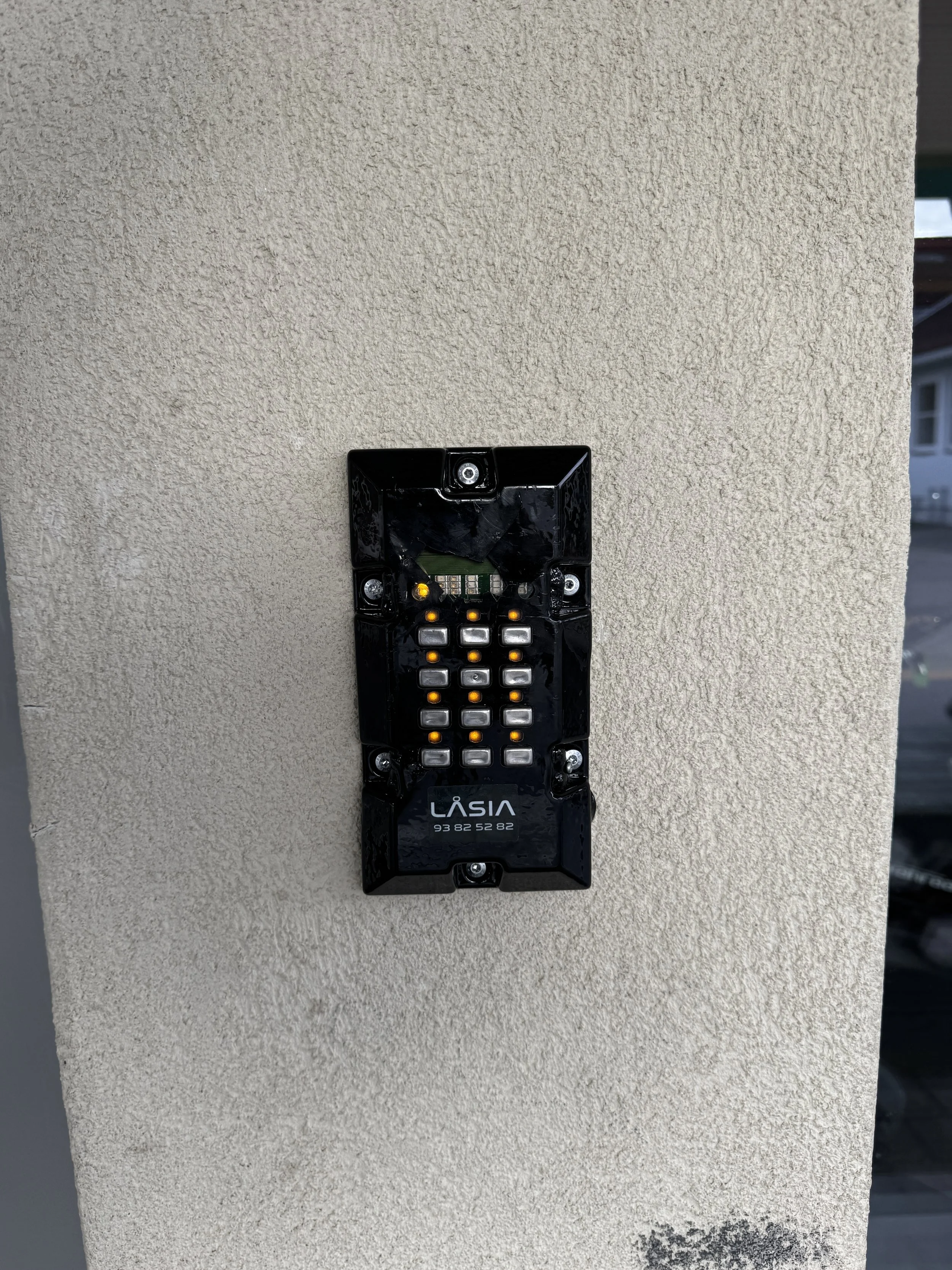 Ukostet utendørs intercom-enhet montert på en beige vegg.