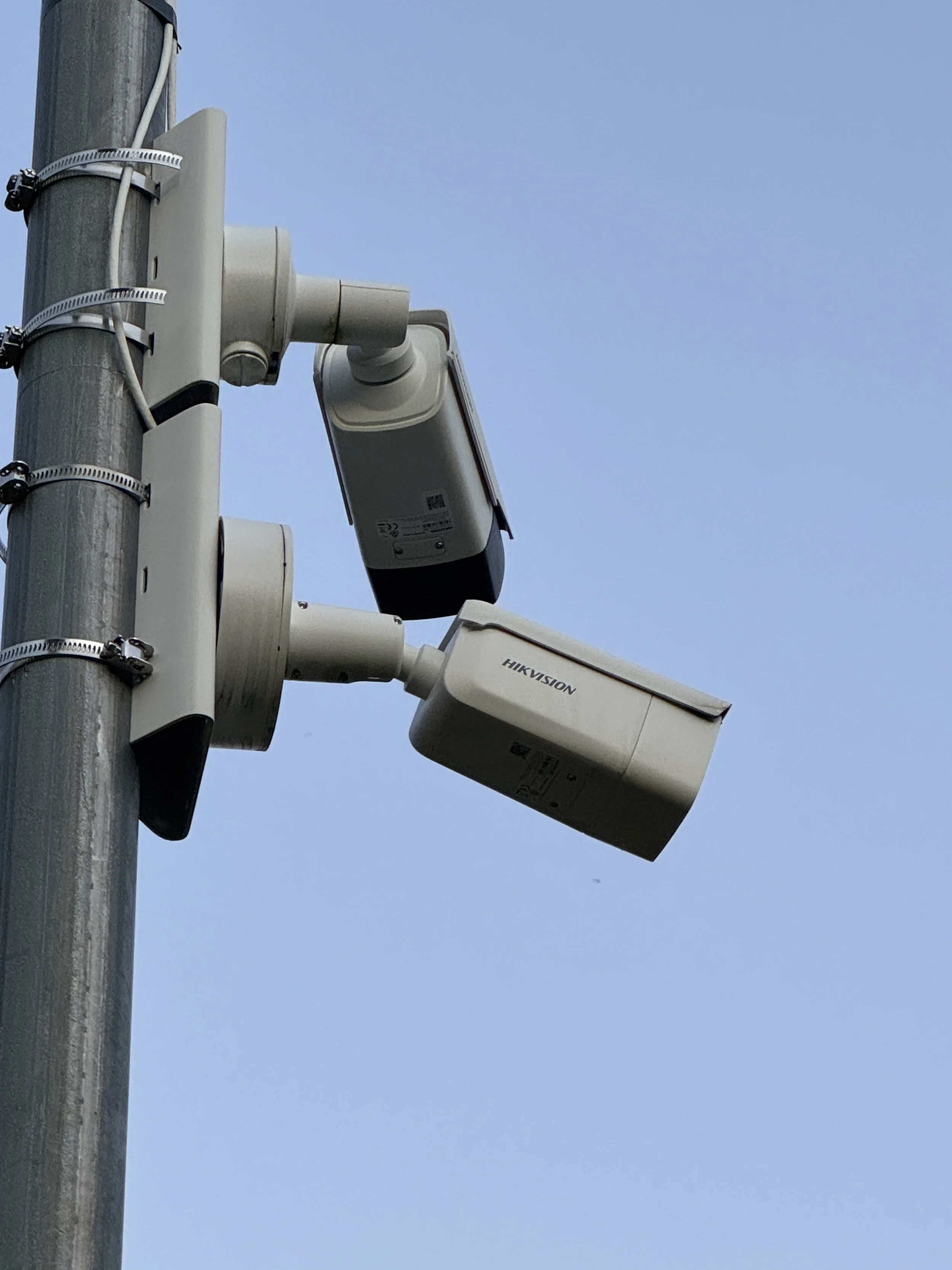 To overvåkingskameraer festet på en lyktestolpe mot en blå himmel.