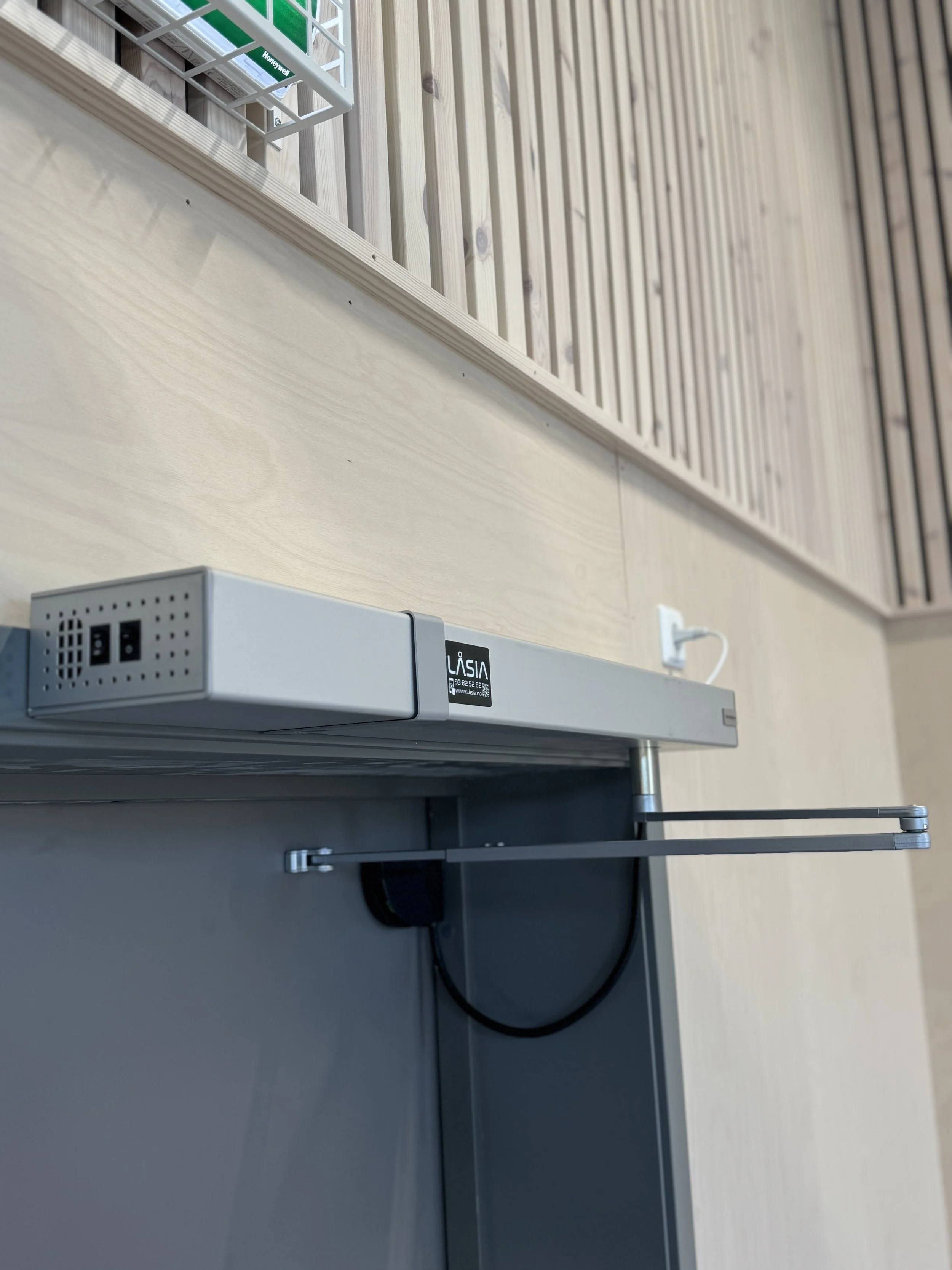 Elektrisk veggkontakt og en metallramme med kabel, plassert på en vegg med vertikale, lyse tremønstre.