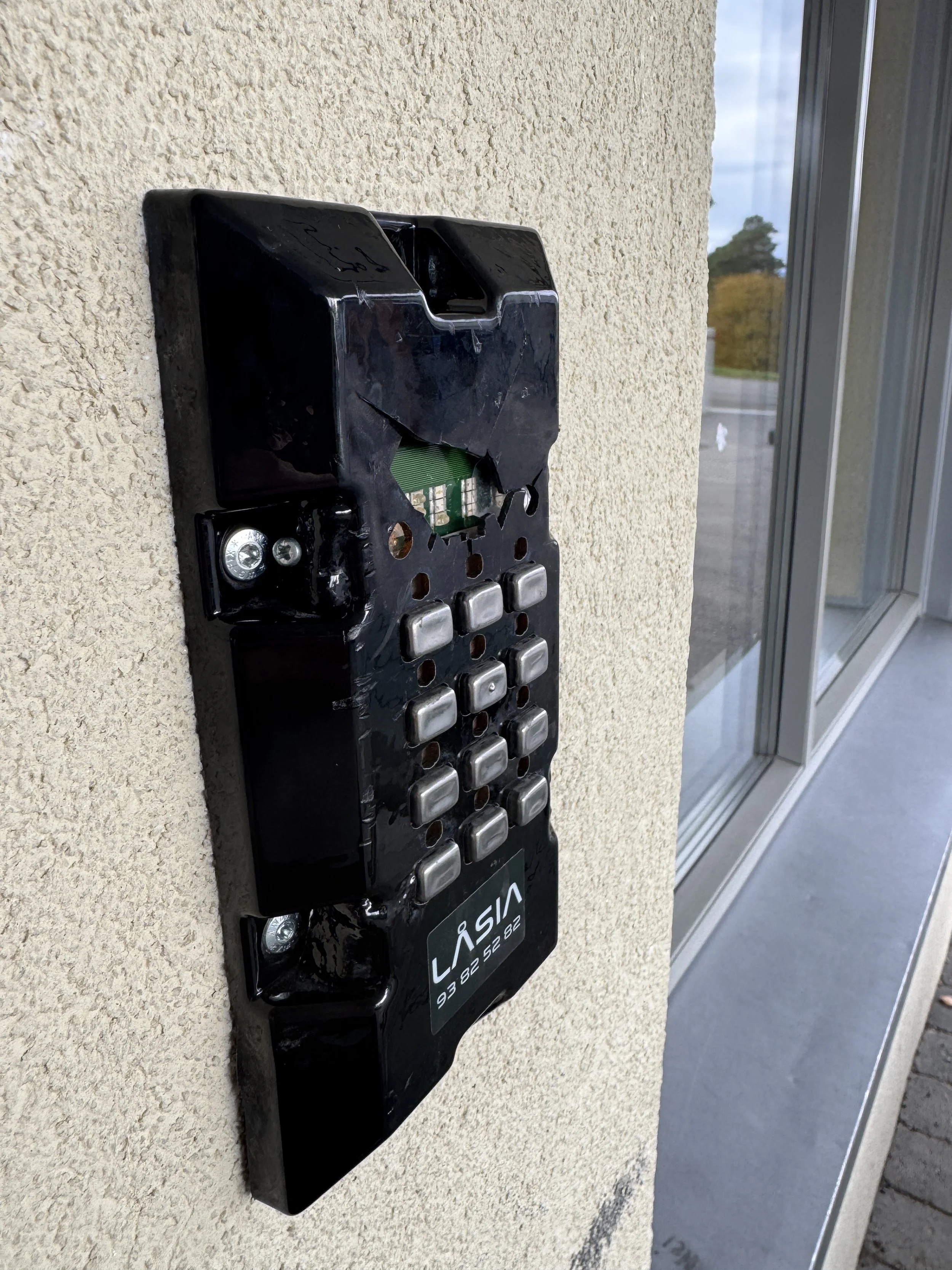 En ufullstendig alarm eller intercomenhet festet på en vegg uten deksler, med merkingen 'LASIA' og en telefonnummer under.