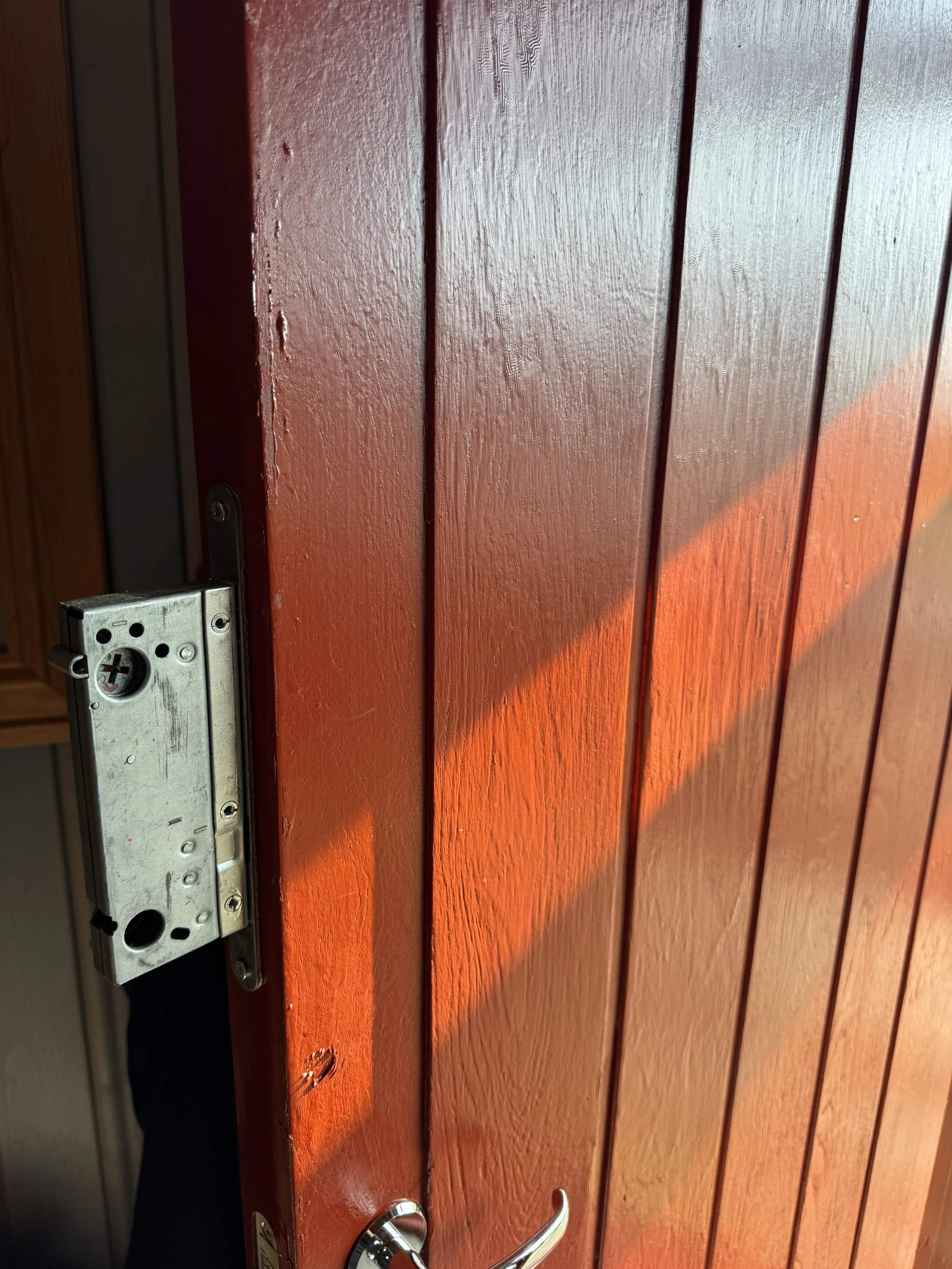 Døren er malt rød og har en metall-lås og dørhåndtak. Det er synlig trepanel på døren.