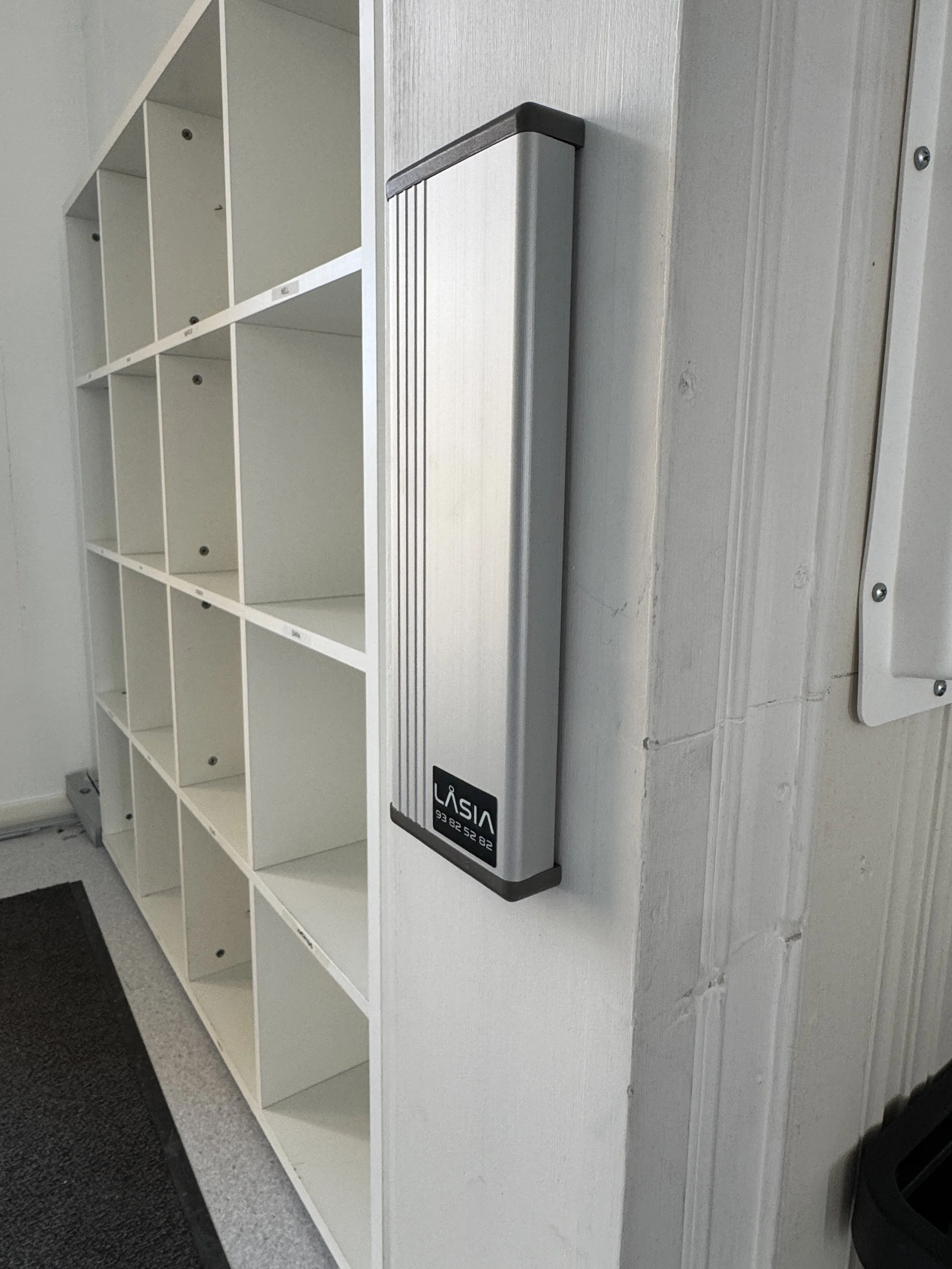 En metallisk lysarmatur montert på en hvit vegg ved en hvit hylleskap.