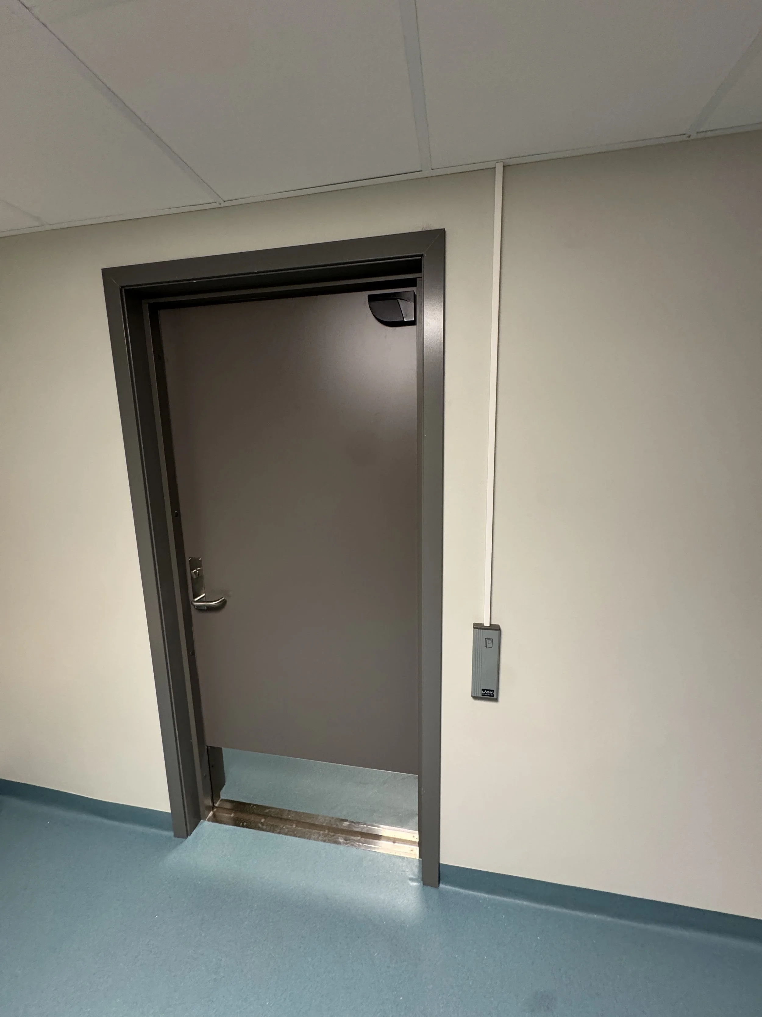 Lukket dørtak av metall i et rom med blågrønn gulvbelegg og hvite vegger.