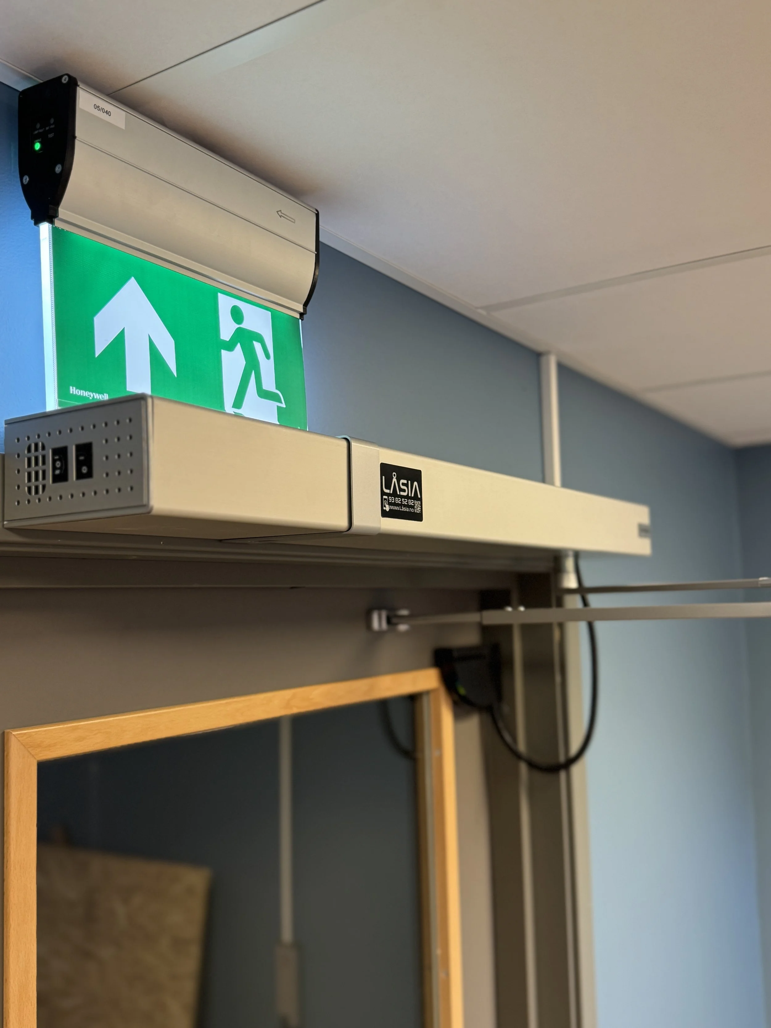 Grønt nødutgangsskilt med pil opp og løpende figur over døren.