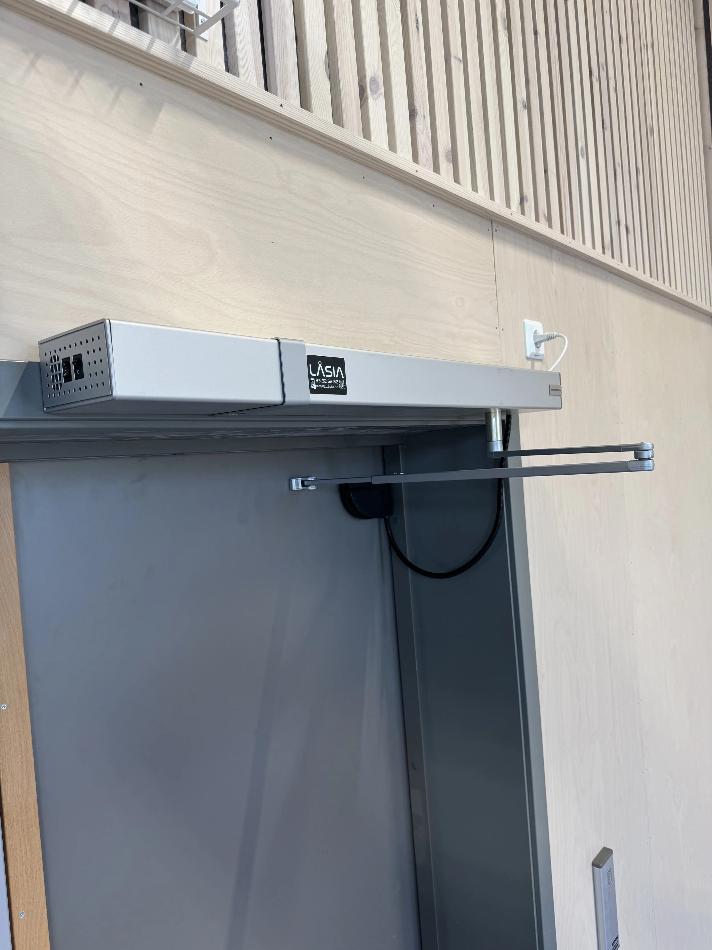 Et metallskilt som viser at døren er automatisert og har en elektrisk lås.