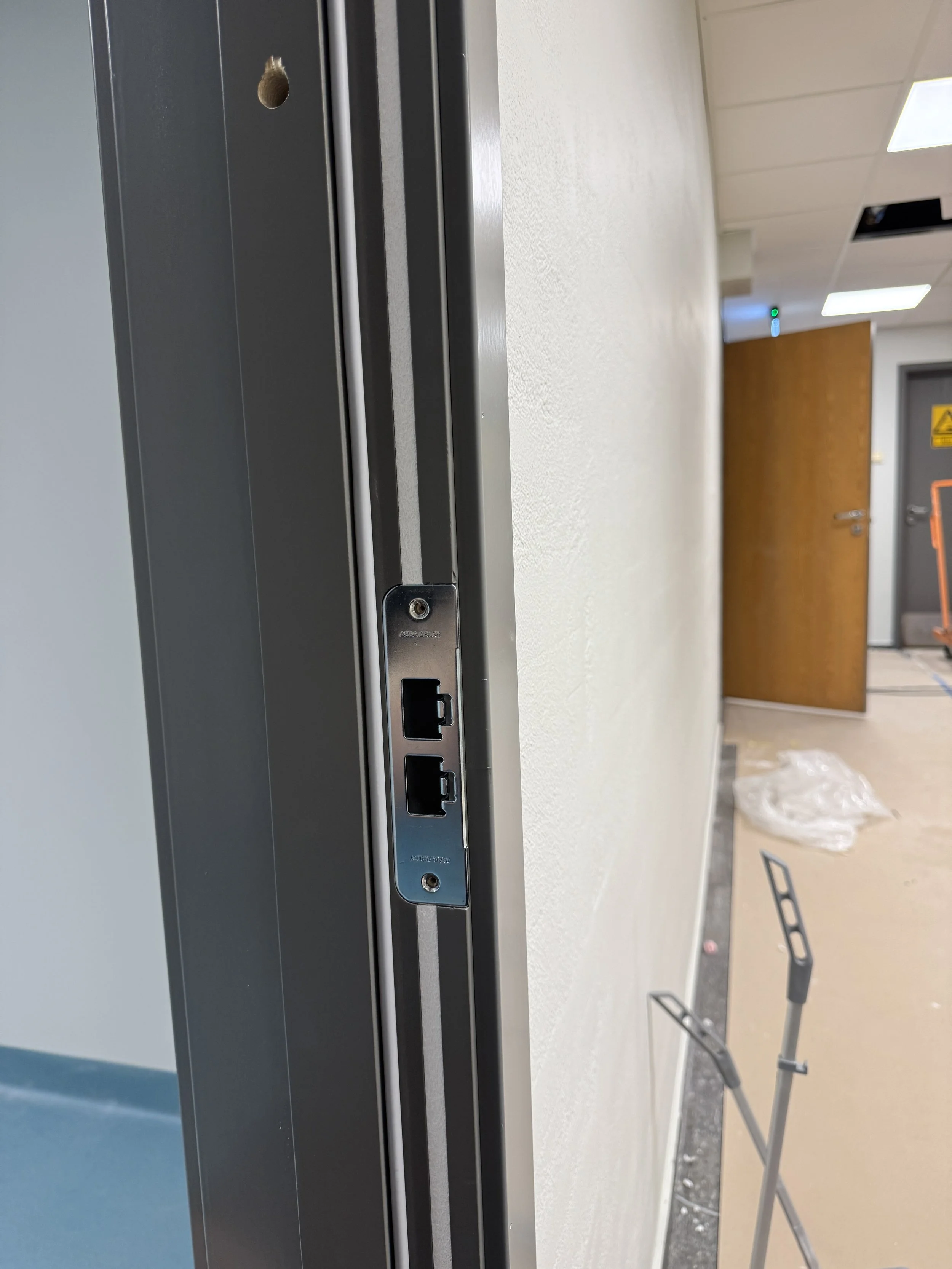 Nærbilde av IT- eller nettverksport tilkoblet på en vegg i et bygg, med en åpen dør og byggearbeidsutstyr synlig i bakgrunnen.