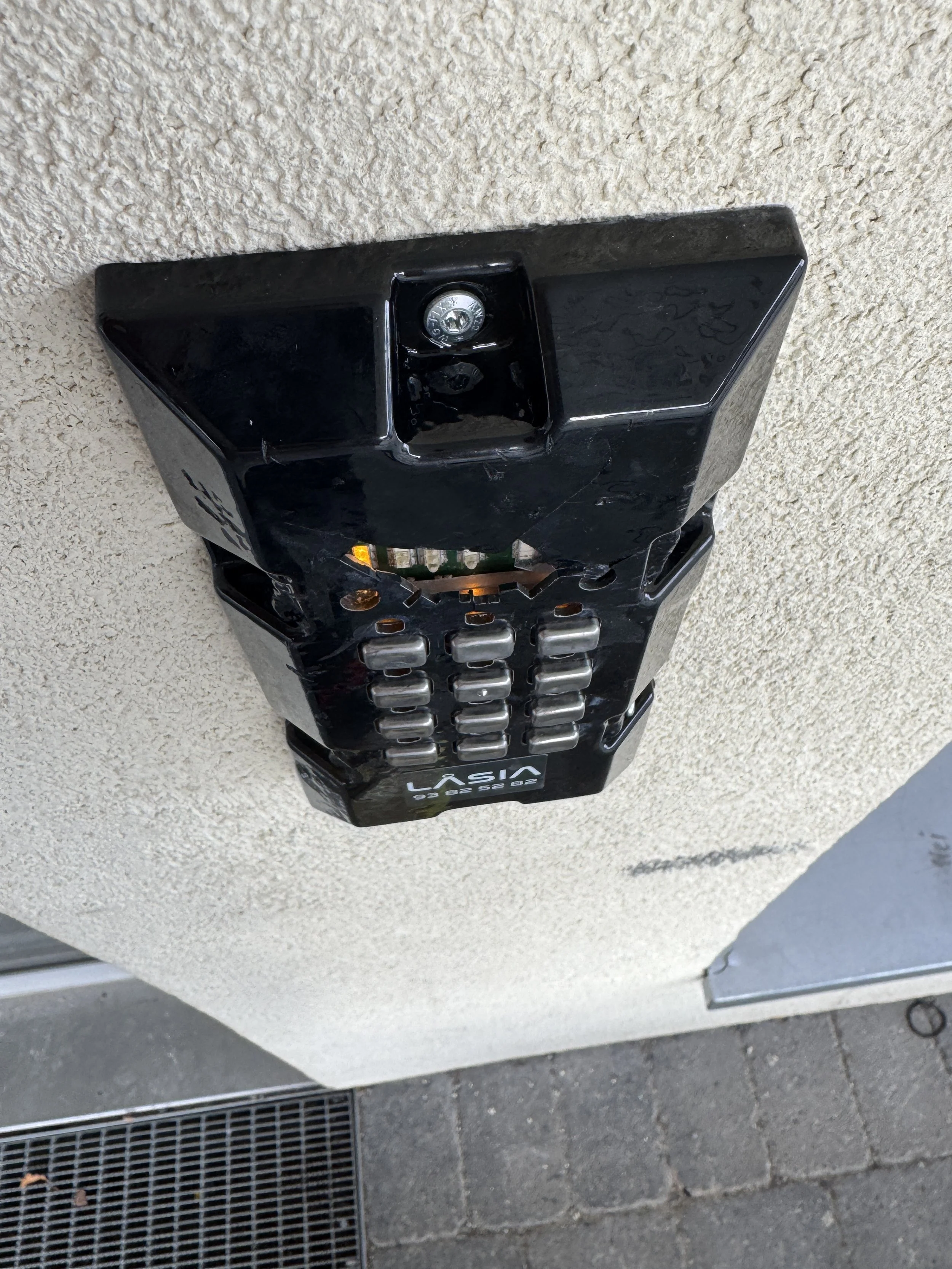 En svartelektronisk låsinstallasjon med tallknapp og kamera, festet på en vegg utendørs.