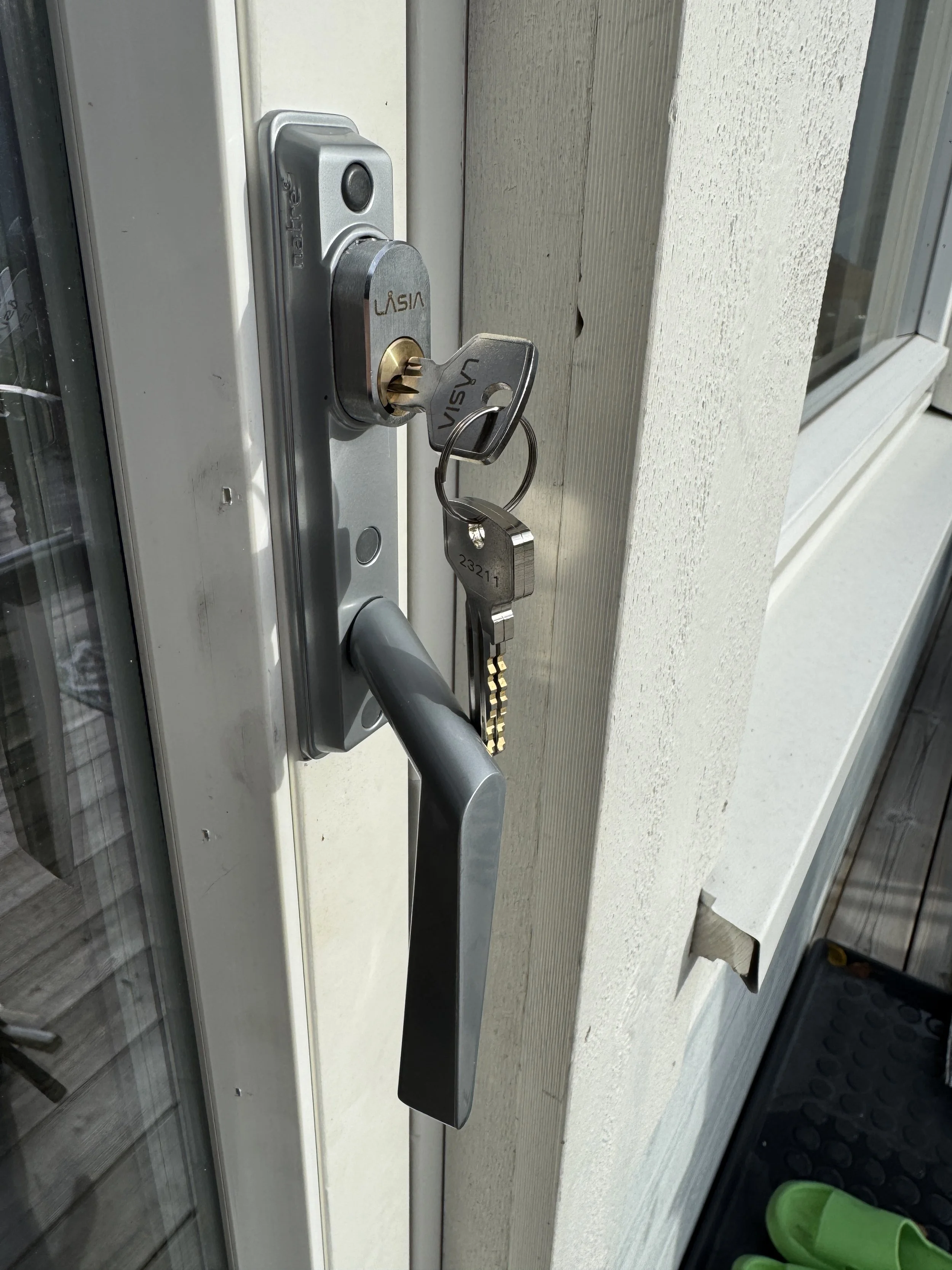 Nærbilde av en inngangsdør med en metallhåndtak og hengelås, med nøkler i låsen.