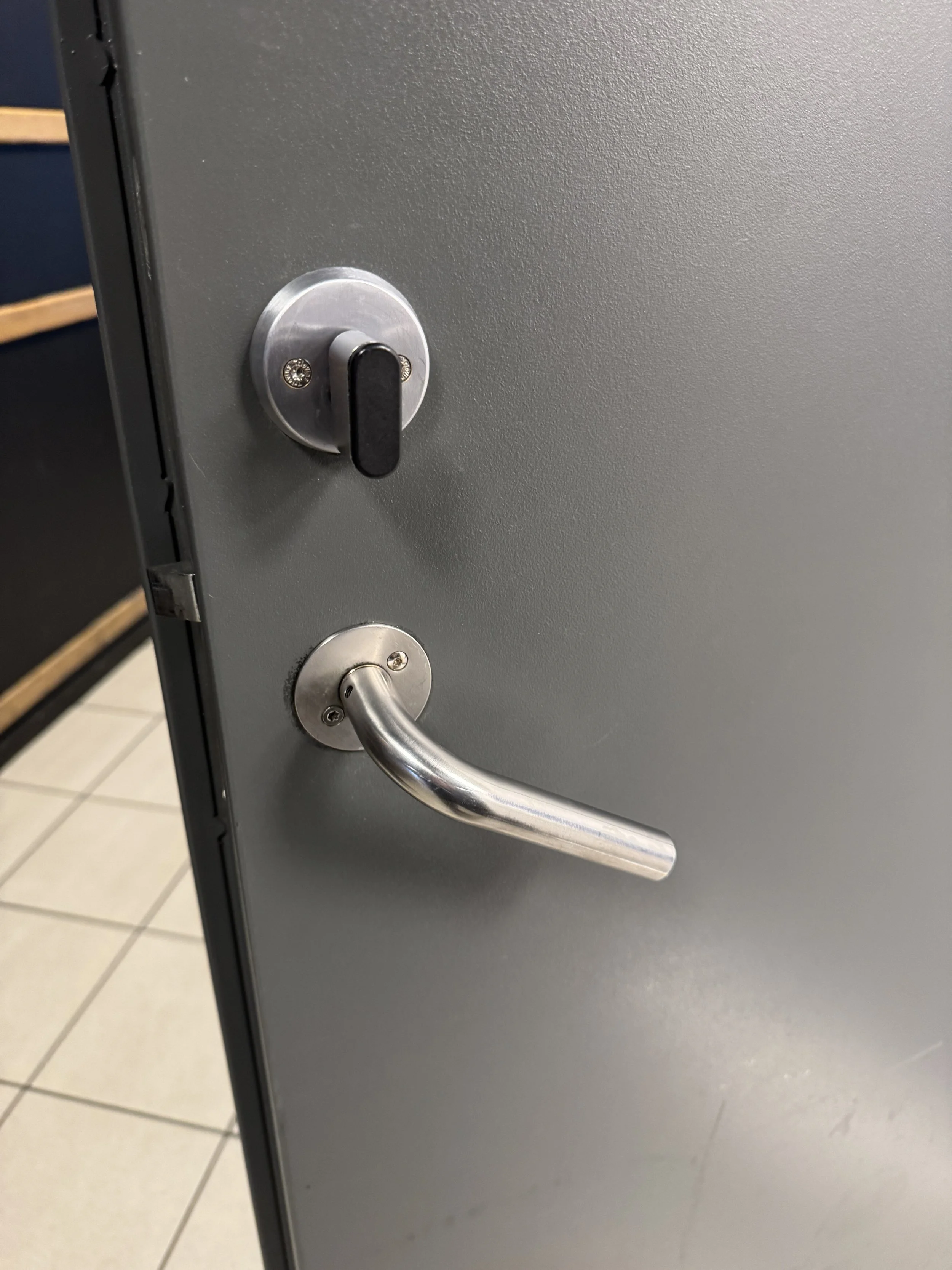 En grå dør med en metallhåndtak og en lås.