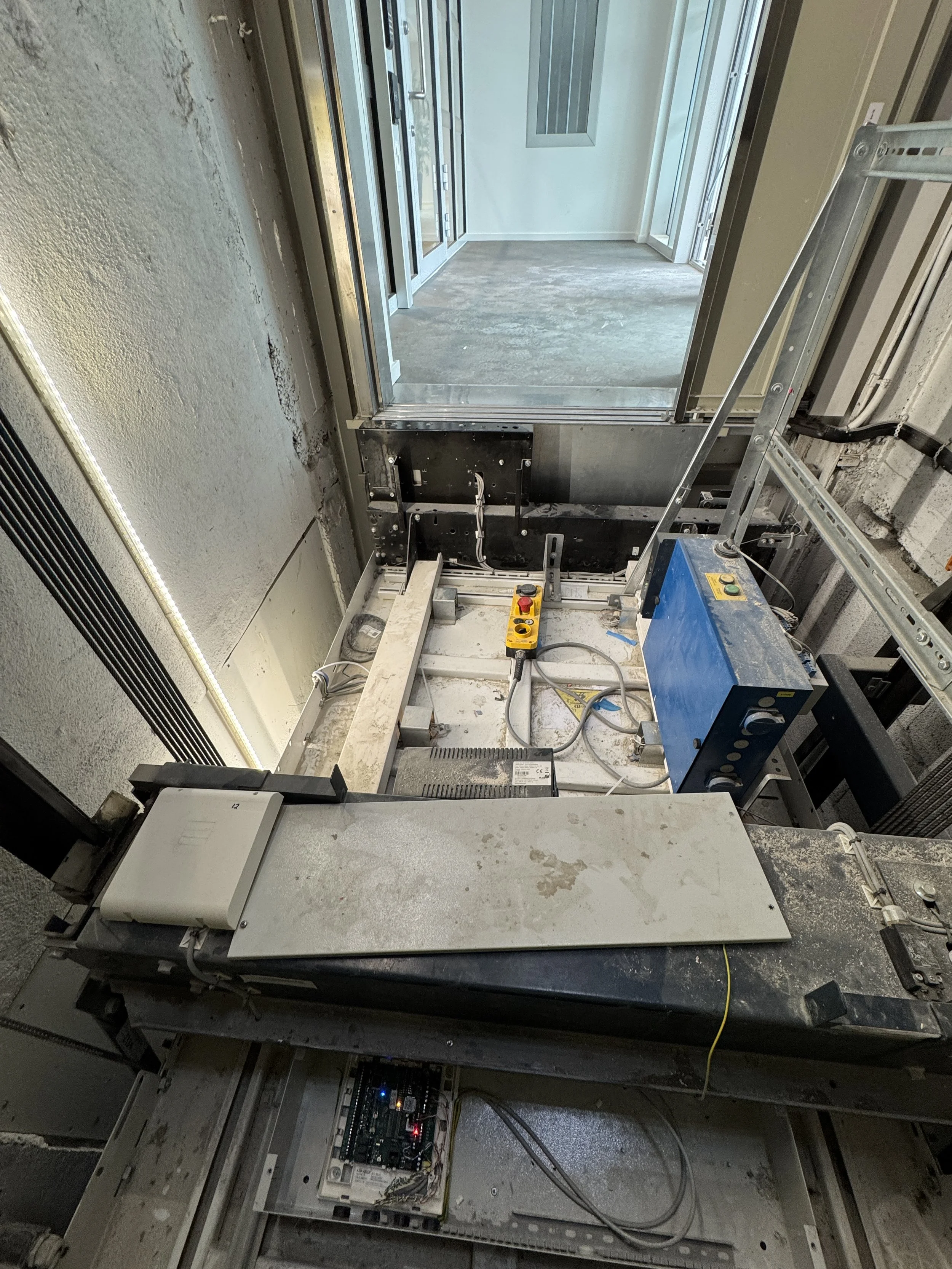 Midlertidig installasjon av heis eller løfteutstyr i et bygg under bygging, med elektrisk kontrollpanel og mekaniske deler.