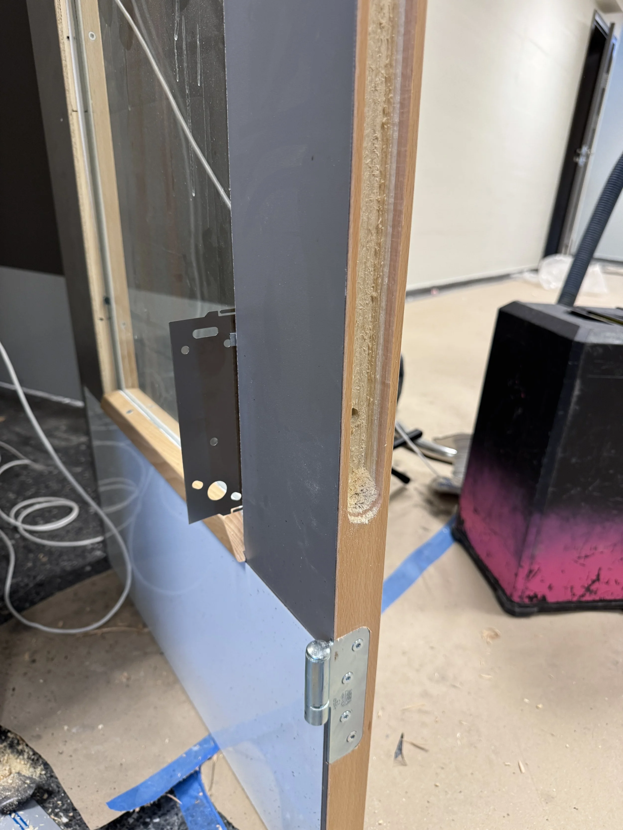 Et delvis montert drikkekar av glass og tre, med synlige beslag og hull i treverket, i et oppussings- eller byggingsmiljø.