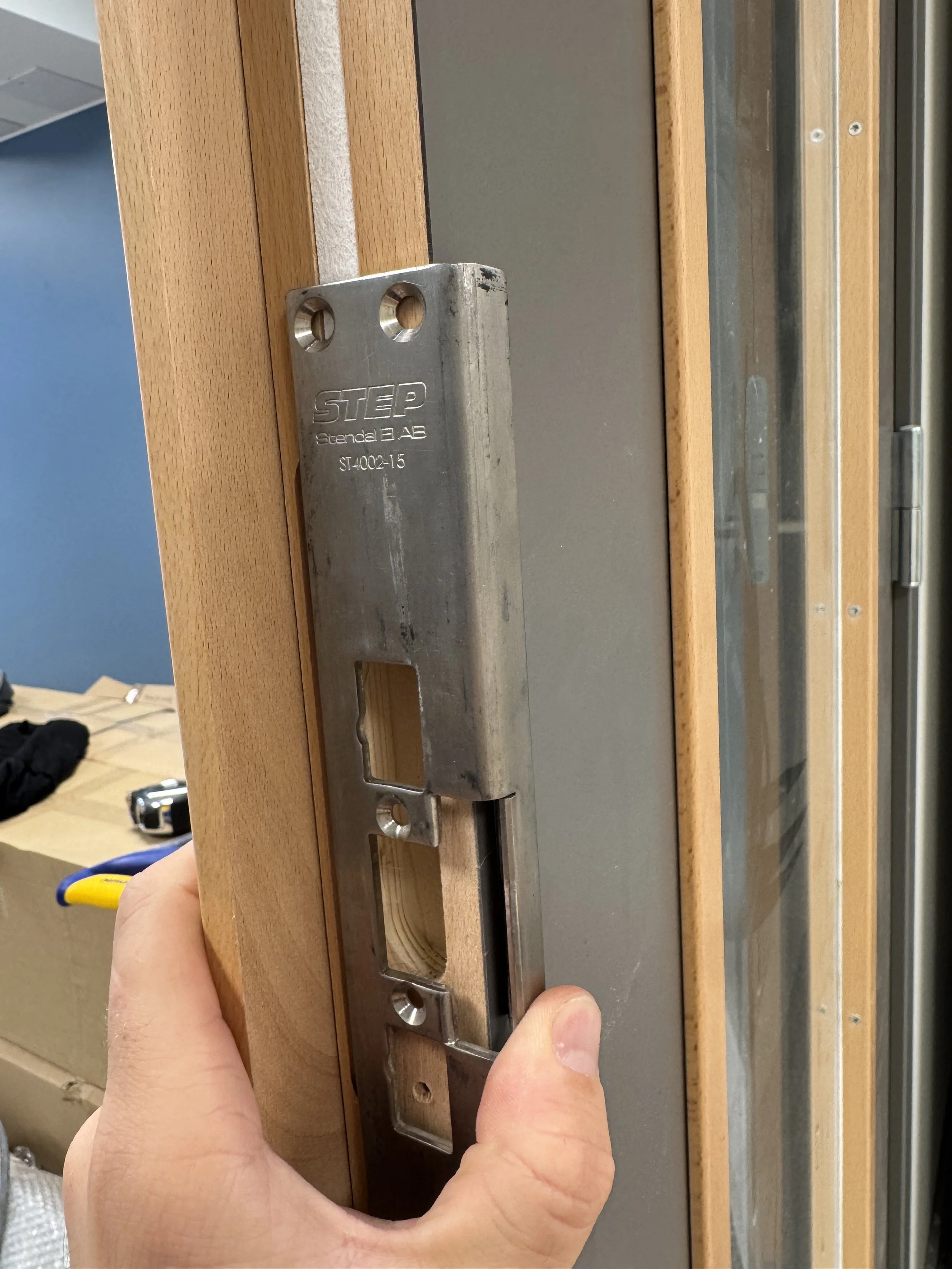 Hånd som holder en metallskinne ved en dørkarm, klar til installasjon.