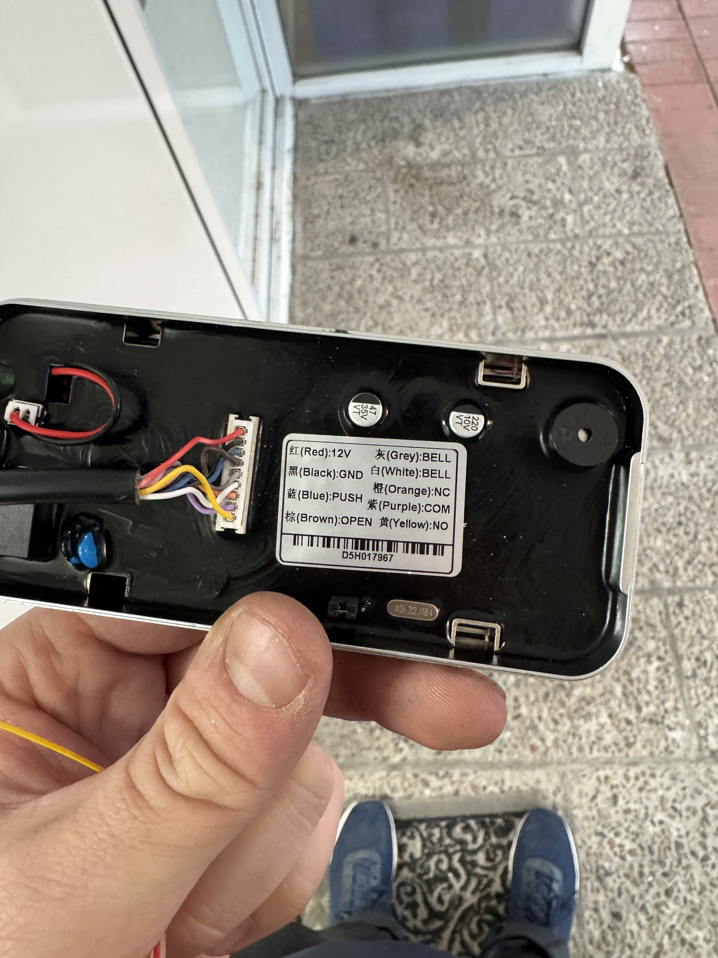 Bilde av innsiden av en elektronisk enhet med en etikett som viser ledningsfargenes funksjoner, plassert i en person som står på en gang med teppe og keramiske fliser, sett ovenfra.