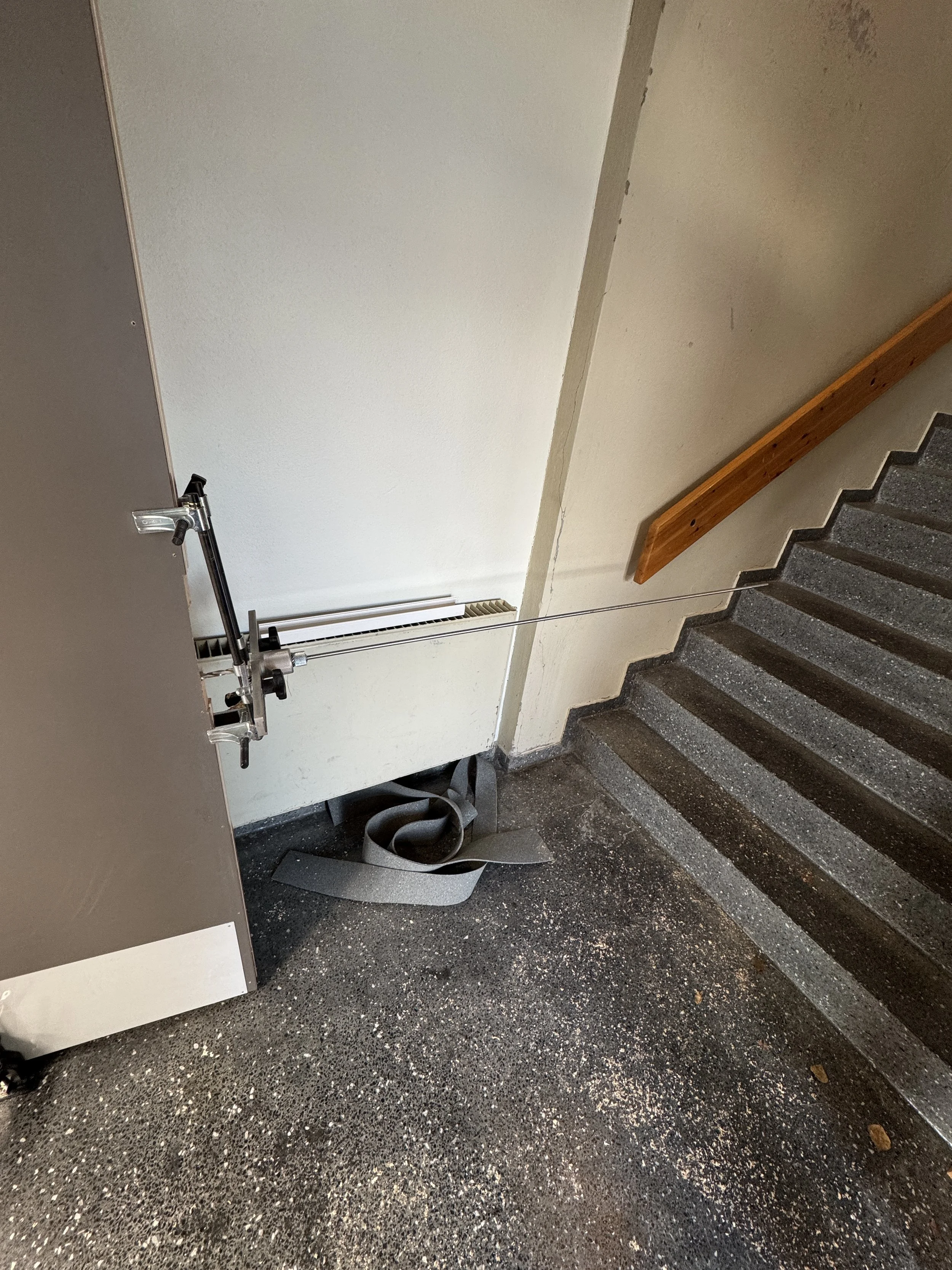 En stålarm med tau og en vekt, plassert ved et canoss-trapp i en bygning.