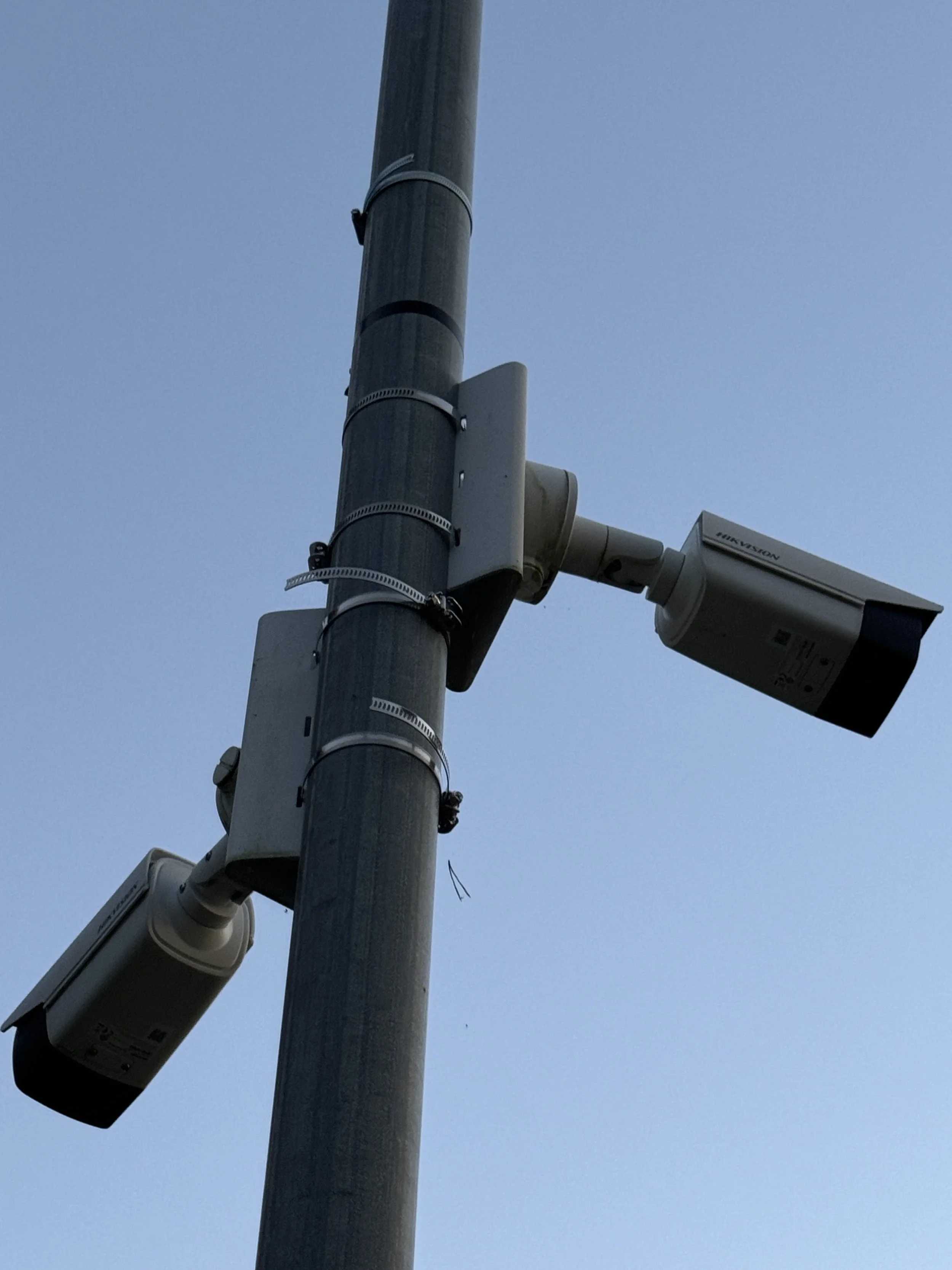 To overvåkingskameraer montert på en vegg mot en klar himmel.