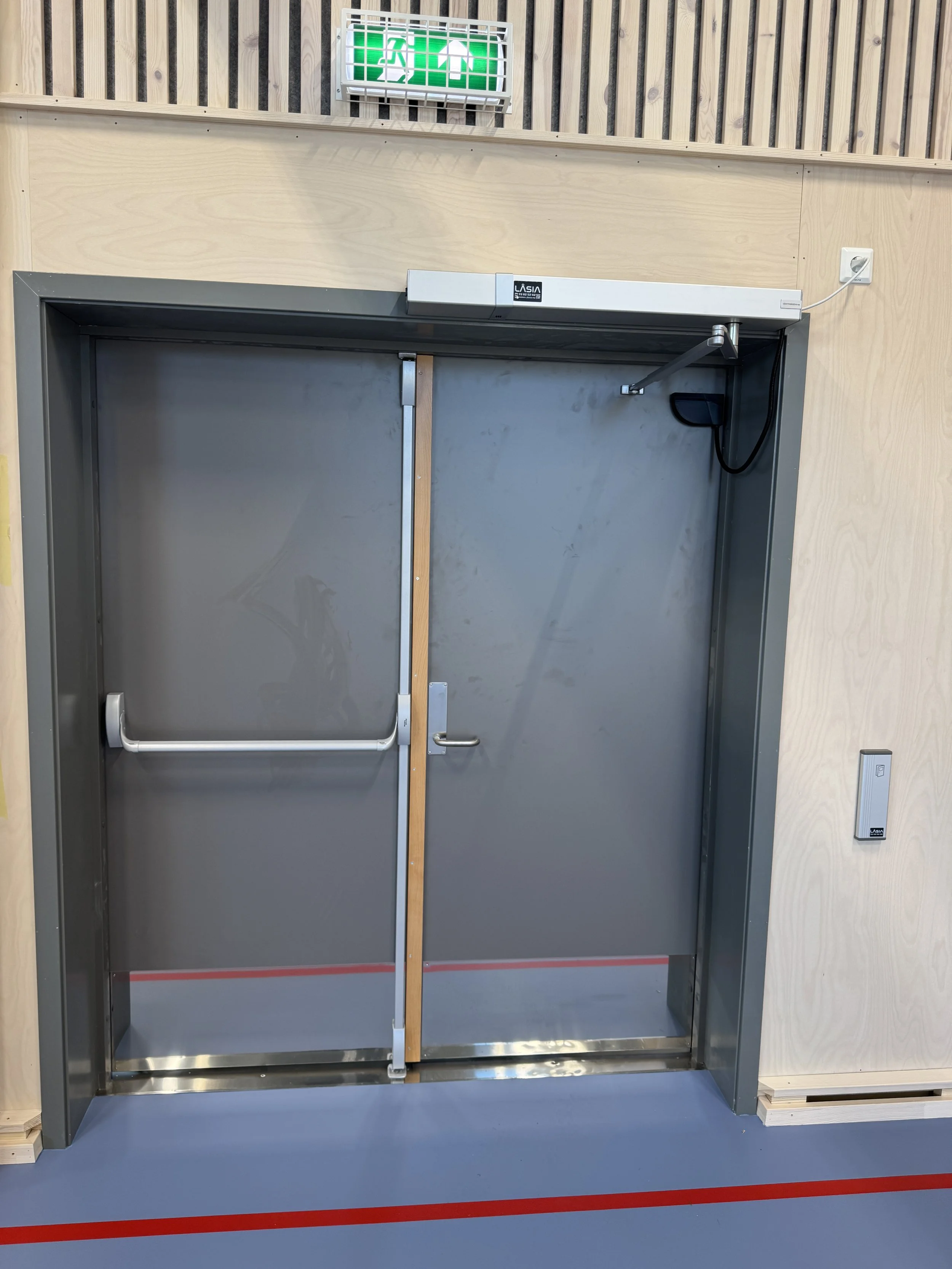 Branddør med nødutgangssignatur over, i et treningsstudio eller hall.