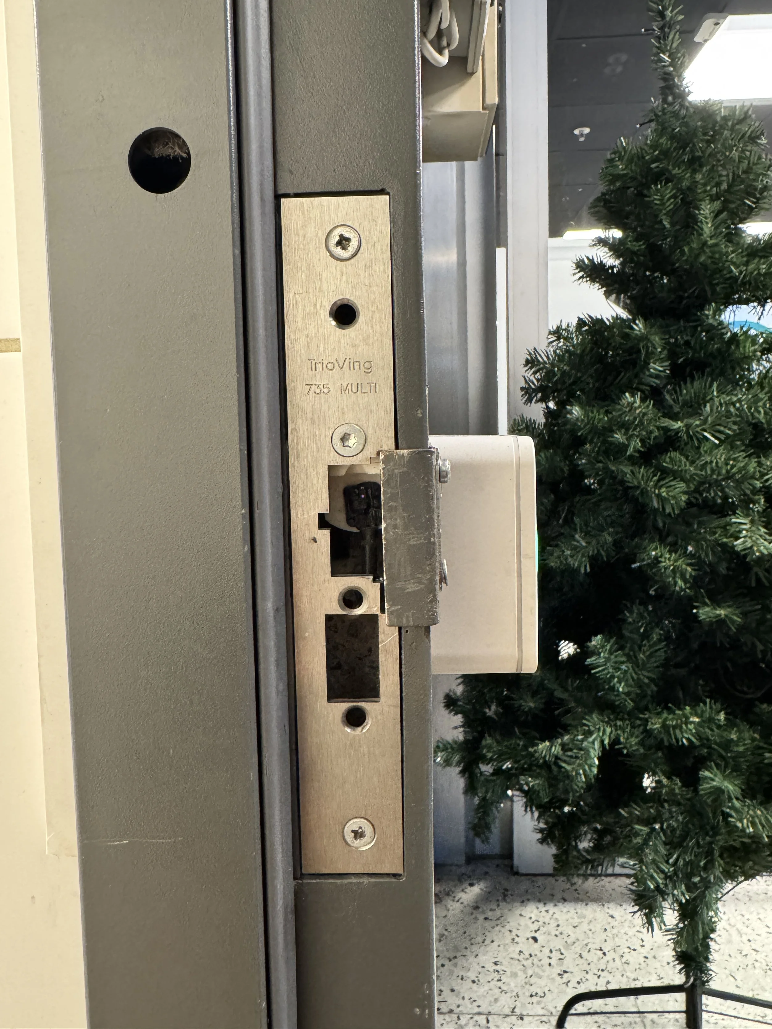 Nærbilde av en dørlås med mekanisme, med en kunstig juletre i bakgrunnen.